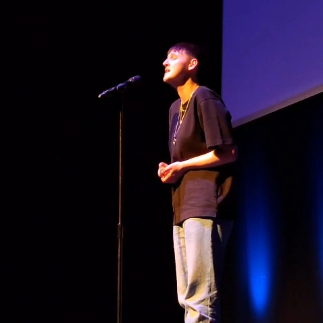 Student performing on stage with mic, blue lighting.