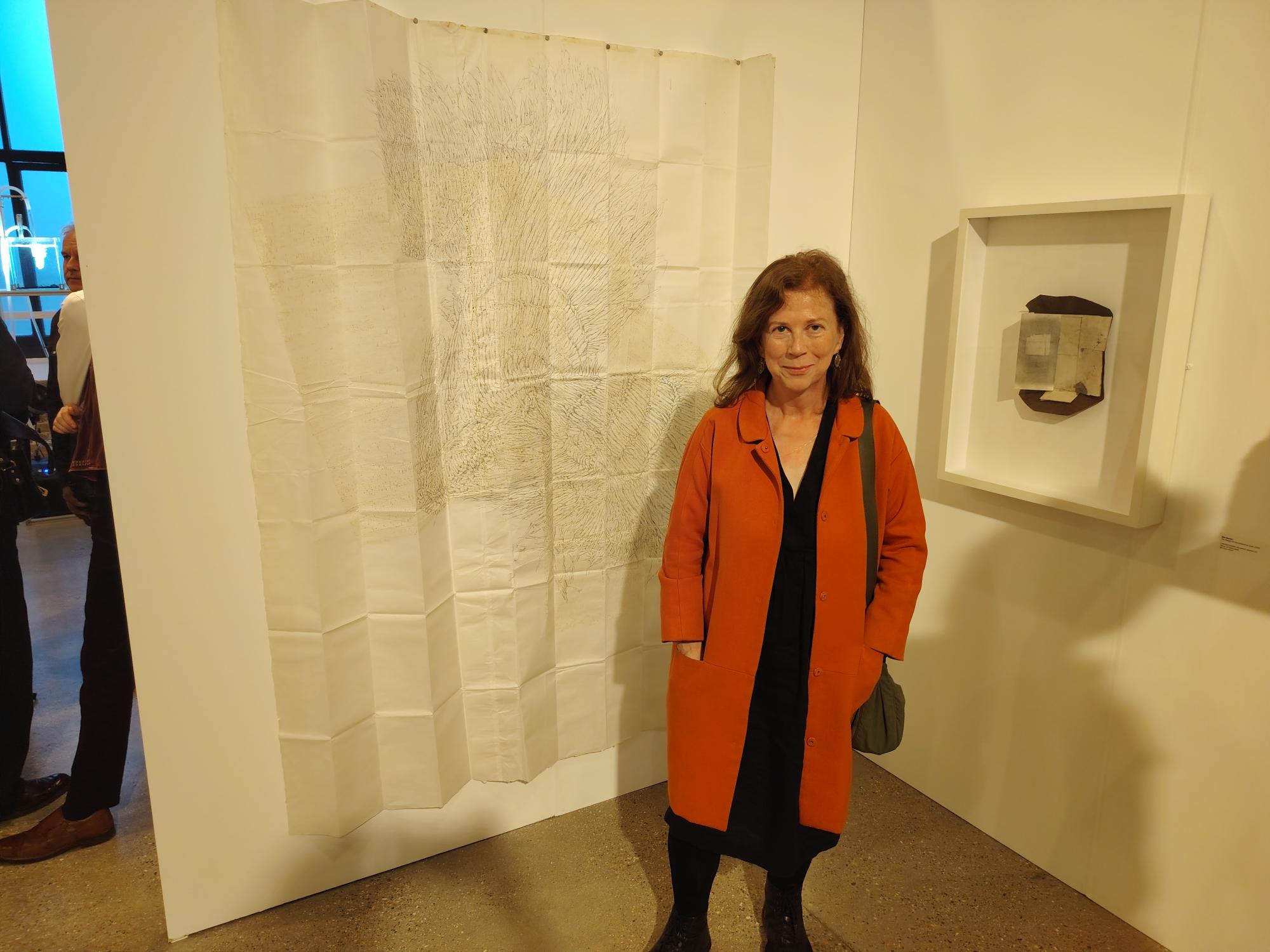 Professor Emerita S Bowen next to one of her drawings on a curtain on display in a gallery.