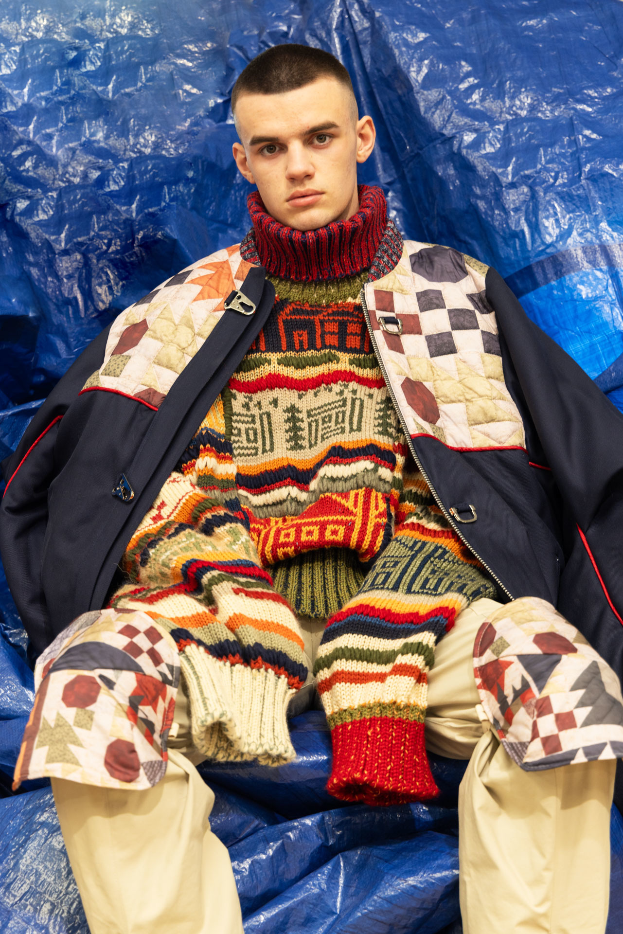 Model dressed in layered, colourful, comfy clothing on a blue background.