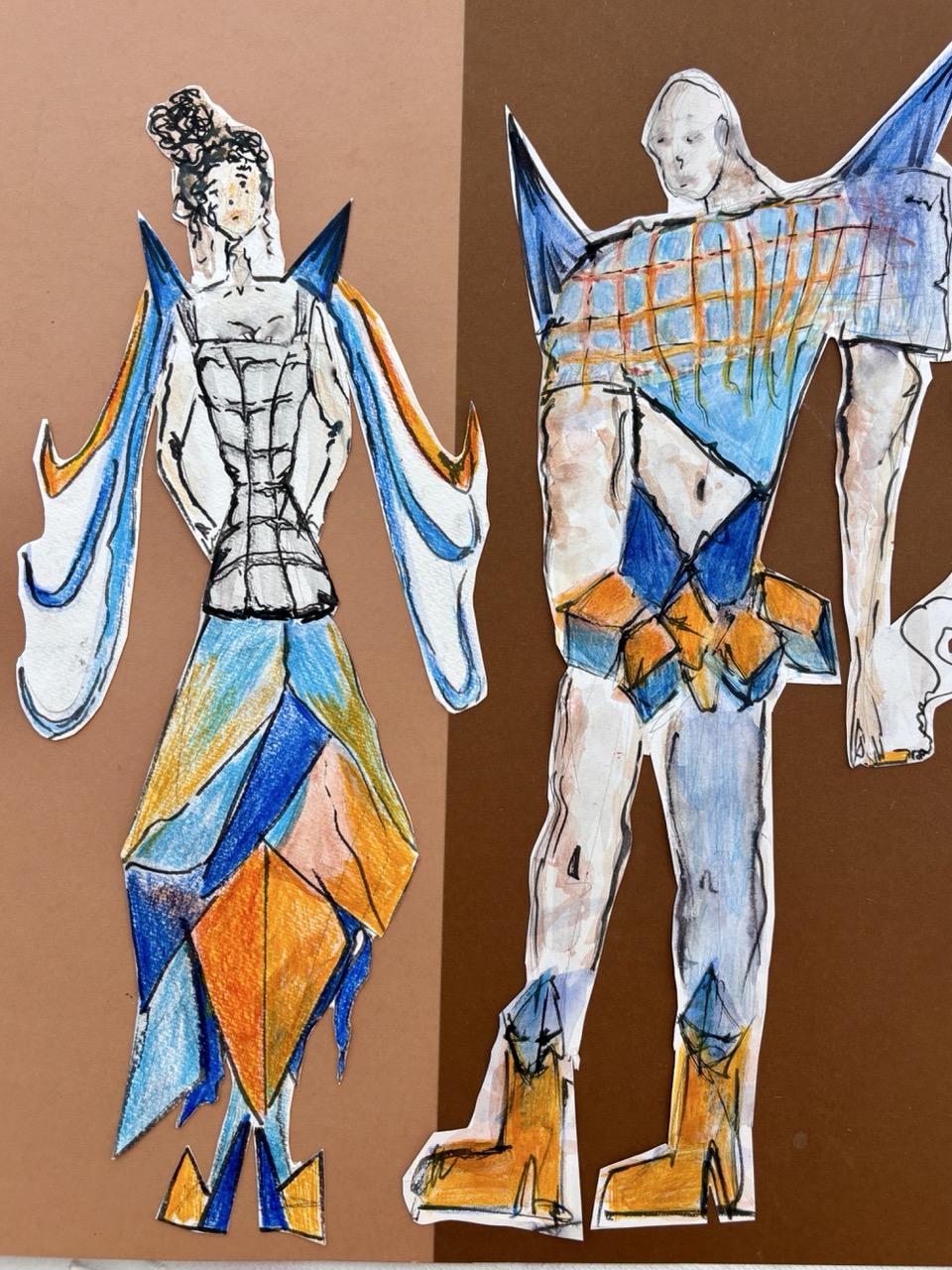 Two colourful paper fashion figures with blue and orange accents are displayed against a brown background.