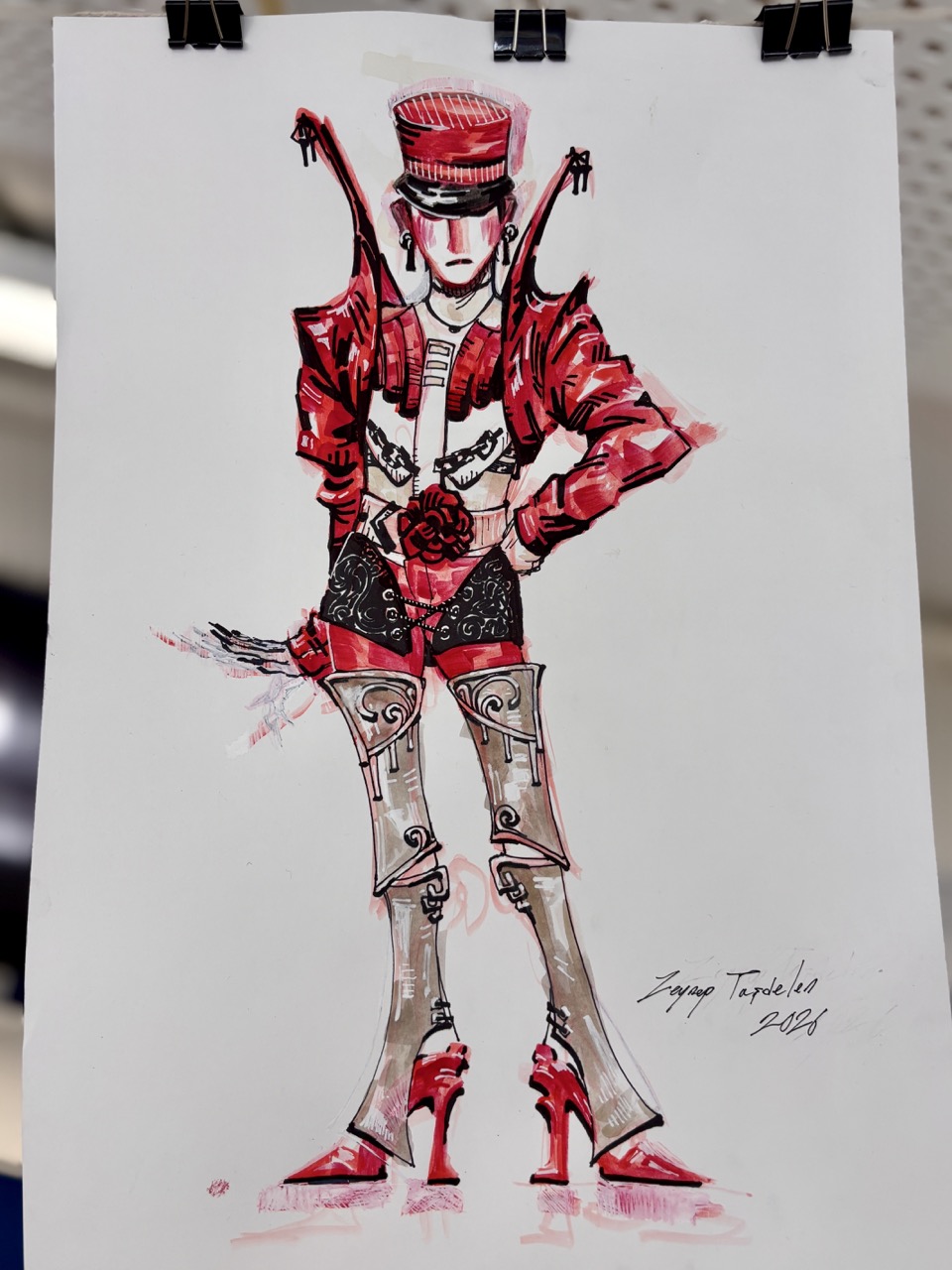 A fashion illustration of a model in a red jacket, black shorts and high heels, drawn on white paper clipped at the top.