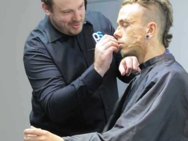 A make-up designer applying prosthetic wounds to a model sitting in a chair.