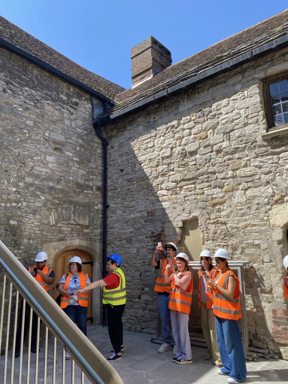 Students in orange hi-vis jackets outside Scaplen's Court, brick wall, blue sky above.