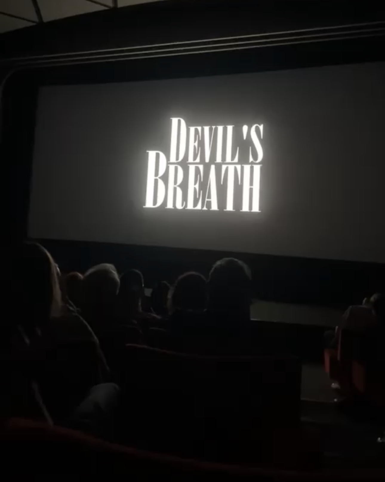 A cinema screen displays the title 'Devil's Breath' above seated audience silhouettes in a dark auditorium.