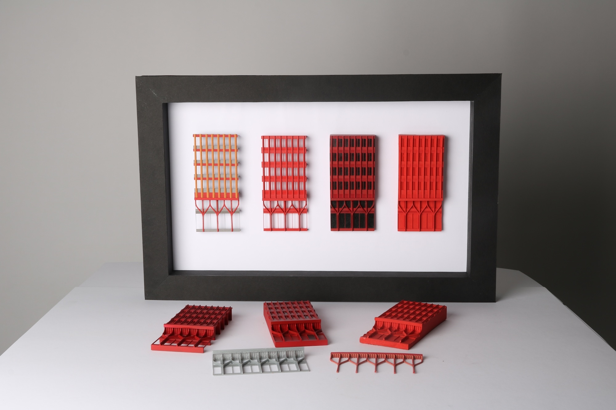 Framed artwork showing four vertical red rectangular sections with grid patterns, displayed with red and grey miniature objects below.
