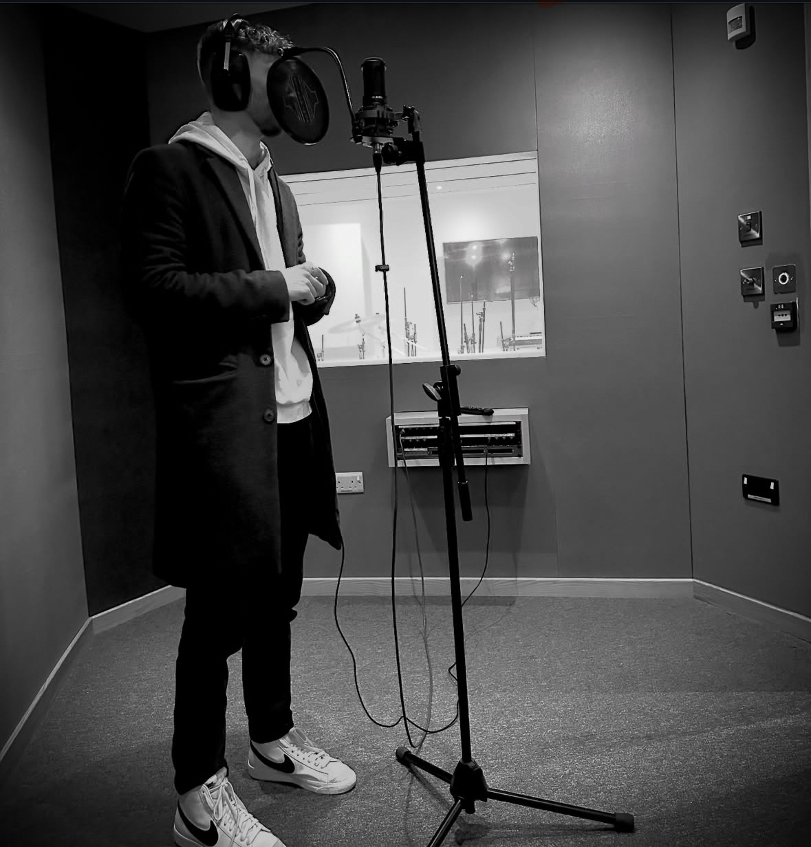 Black and white photo showing E Horne (Spectator) standing in front of a tall microphone stand in a recording booth.