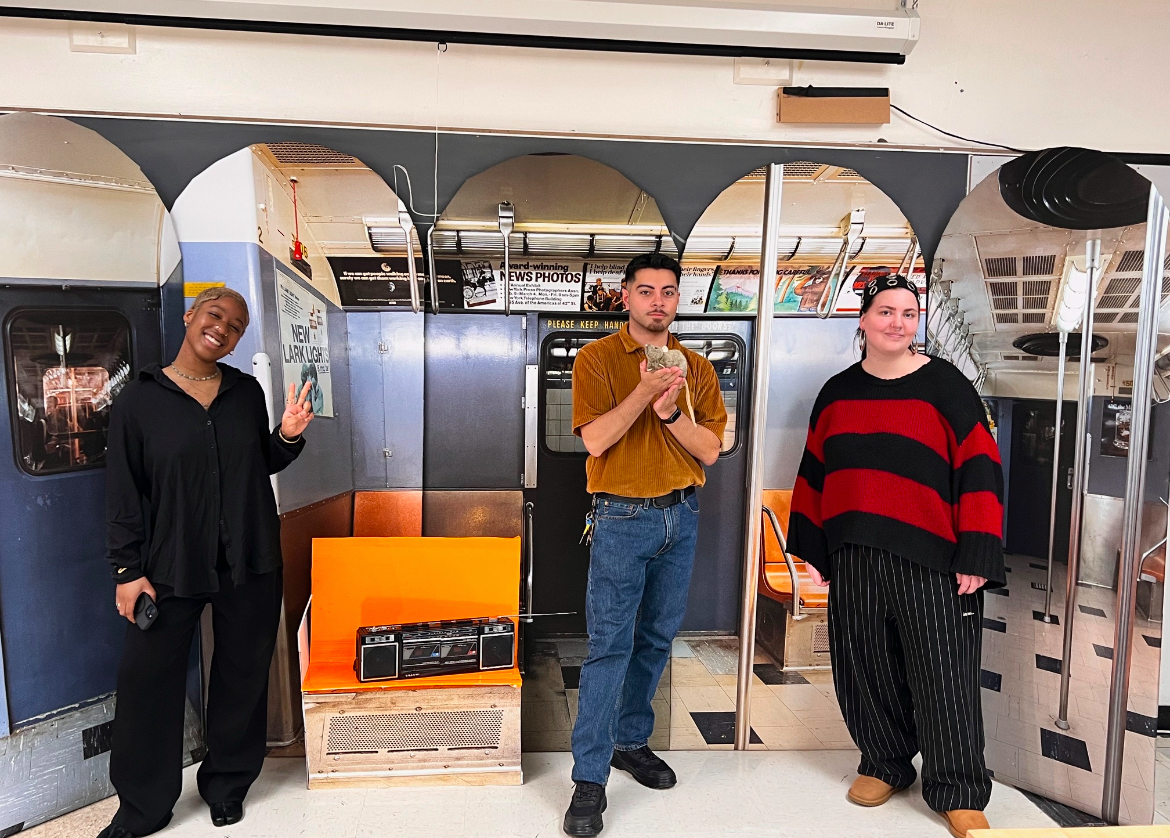 Three people standing in modern kitchen with stainless steel appliances, orange accents, and arched design elements.