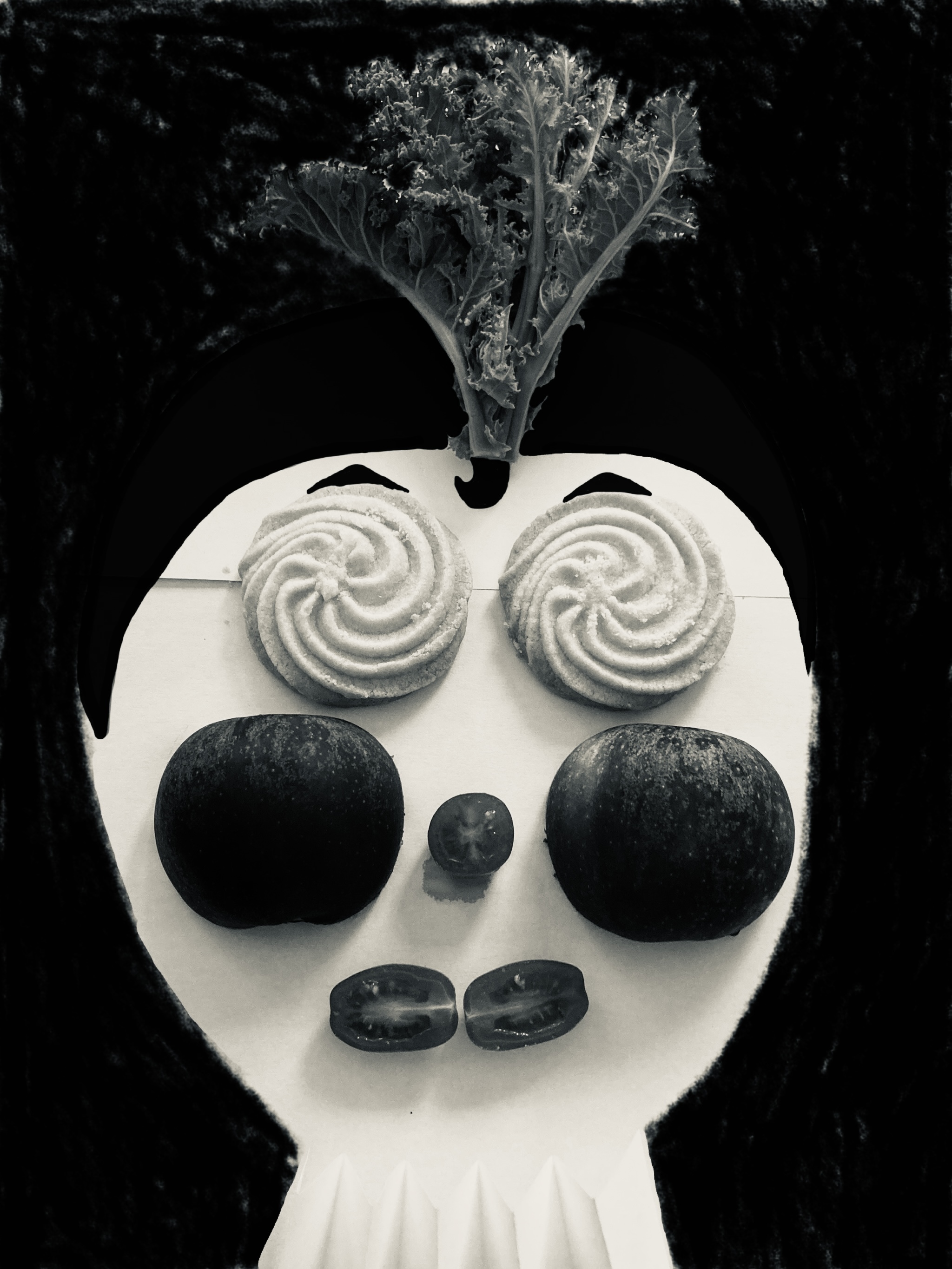 White skull-shaped object with spiral cream designs as eyes, dark green stones as eye sockets and nose, kale leaf sprouting from top.