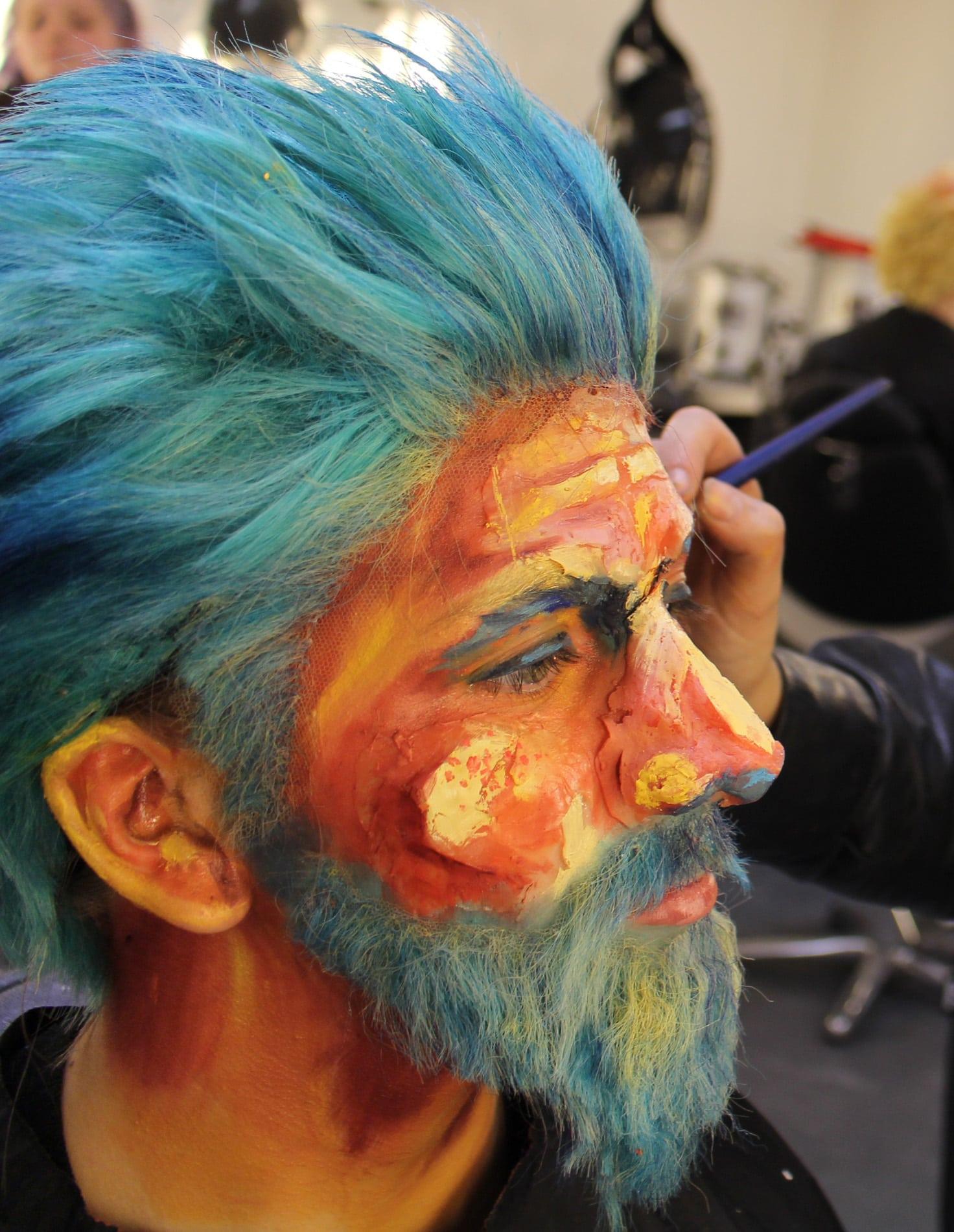 Man wearing orange make-up with blue hair