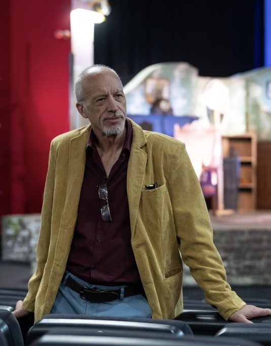Portrait of S Aita working in a theatre, with a stage and set blurred in the background.