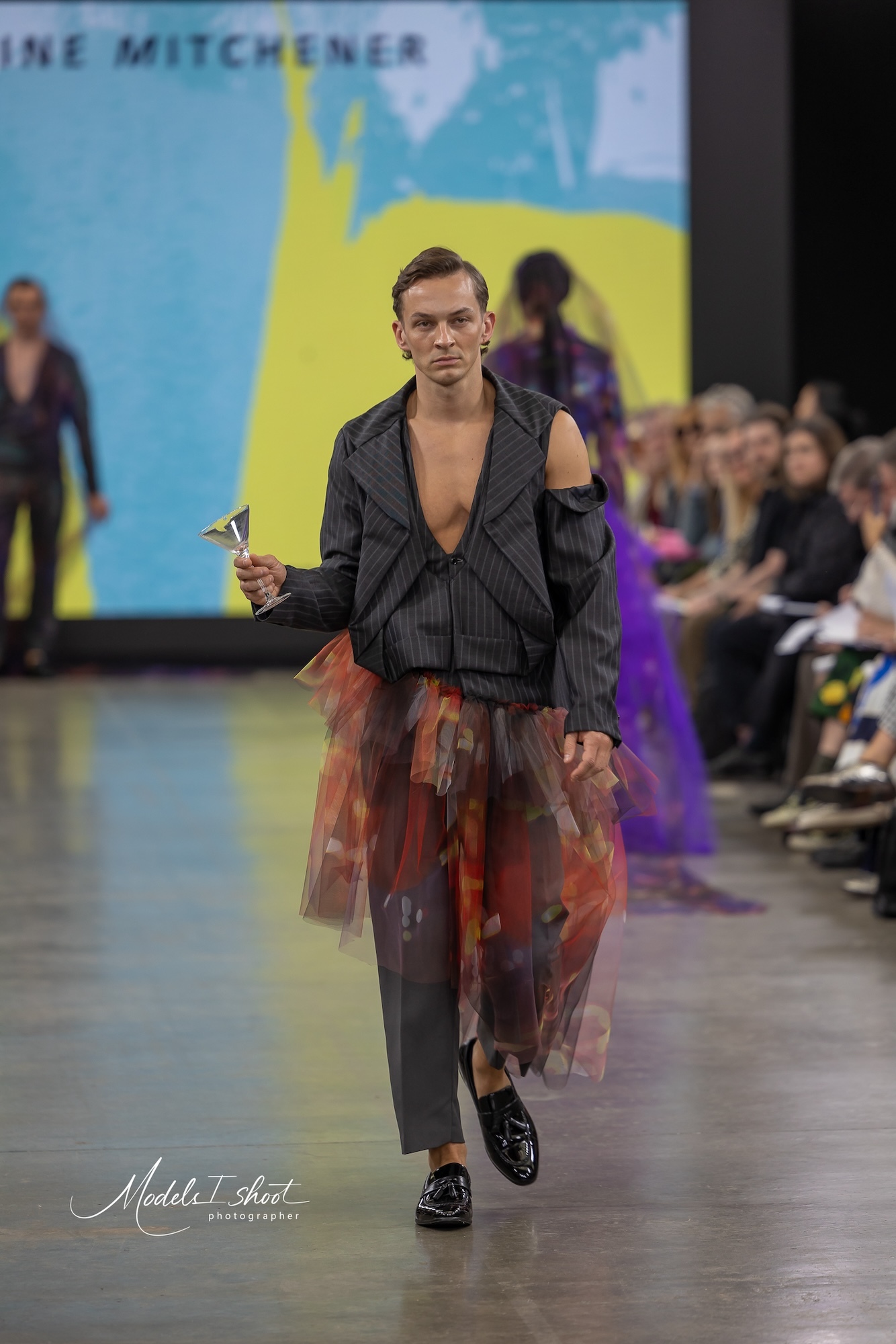 A model wearing a low-cut pinstripe top and trousers and a colourful gauze skirt walks down the catwalk at GFW 2024.