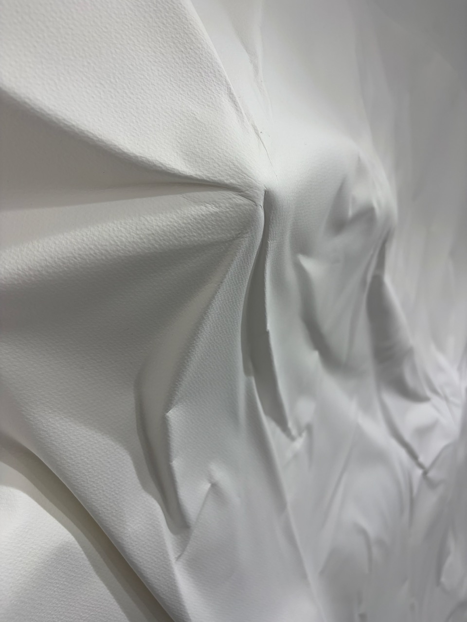 A close-up of crumpled white textured fabric or paper with deep folds and creases.