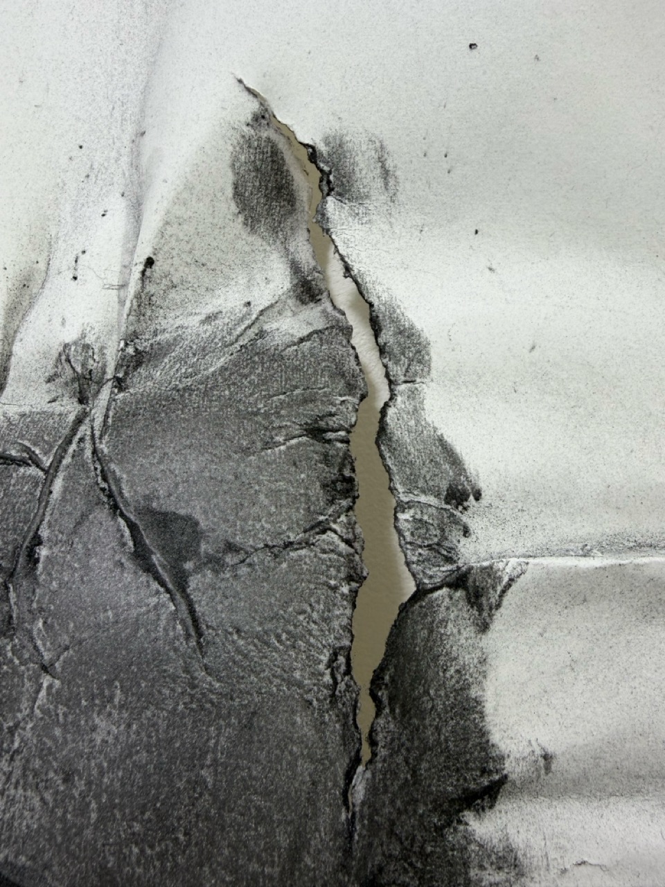 Close-up of a torn white surface with a long vertical split and dark grey scuff marks.
