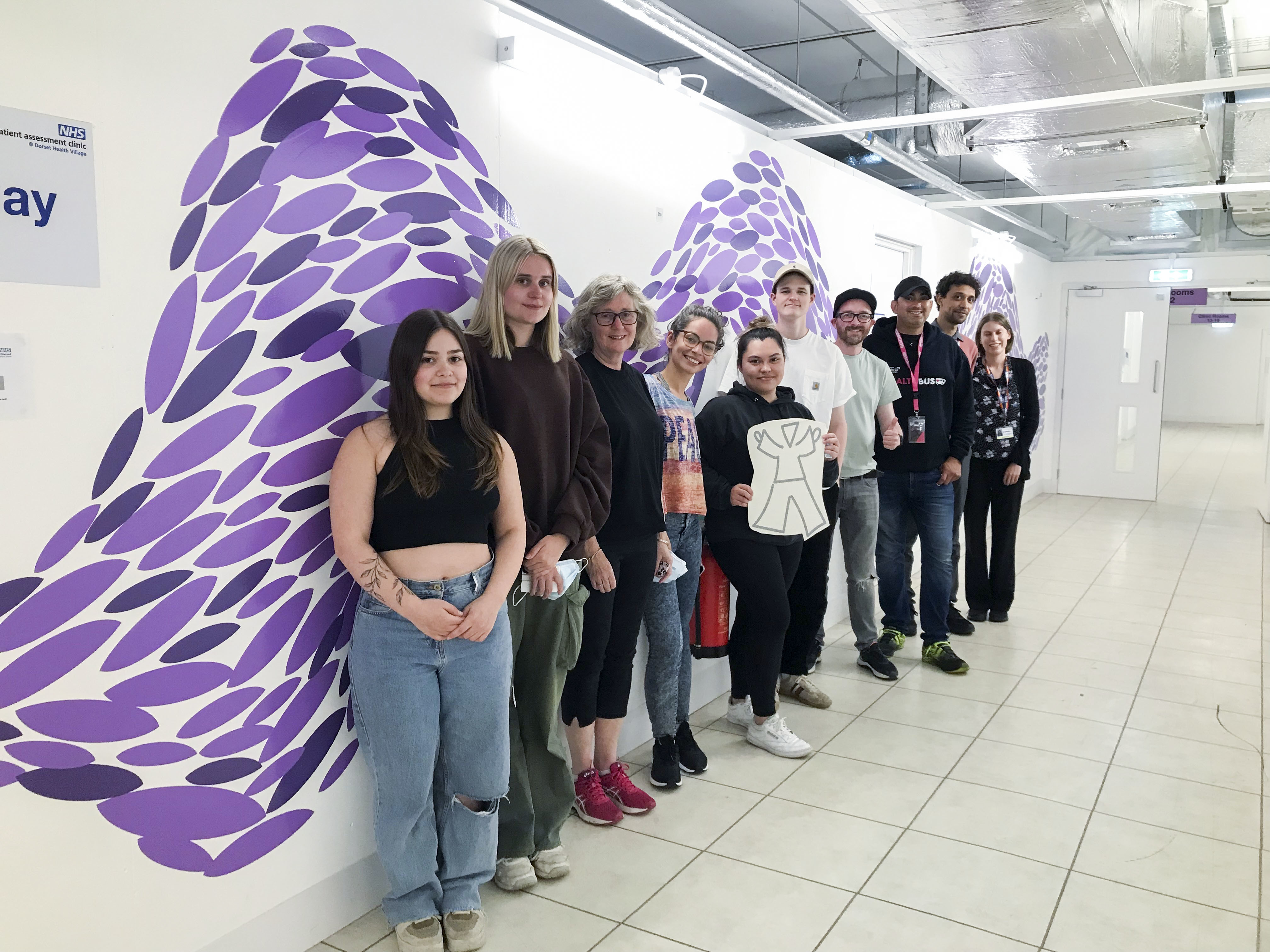 Interior Architecture and Design students at the Outpatients Assessment Centre in Poole. Viewed from a diagonal, a group of people lines up and poses for a photo.