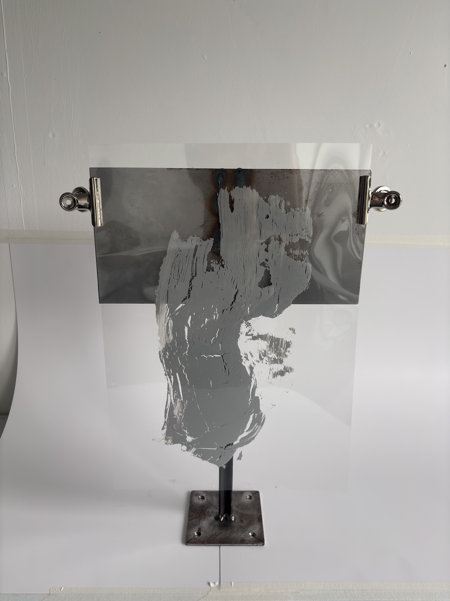 A transparent acrylic art panel with a grey abstract paint print, mounted on a black metal stand against a plain white backdrop.