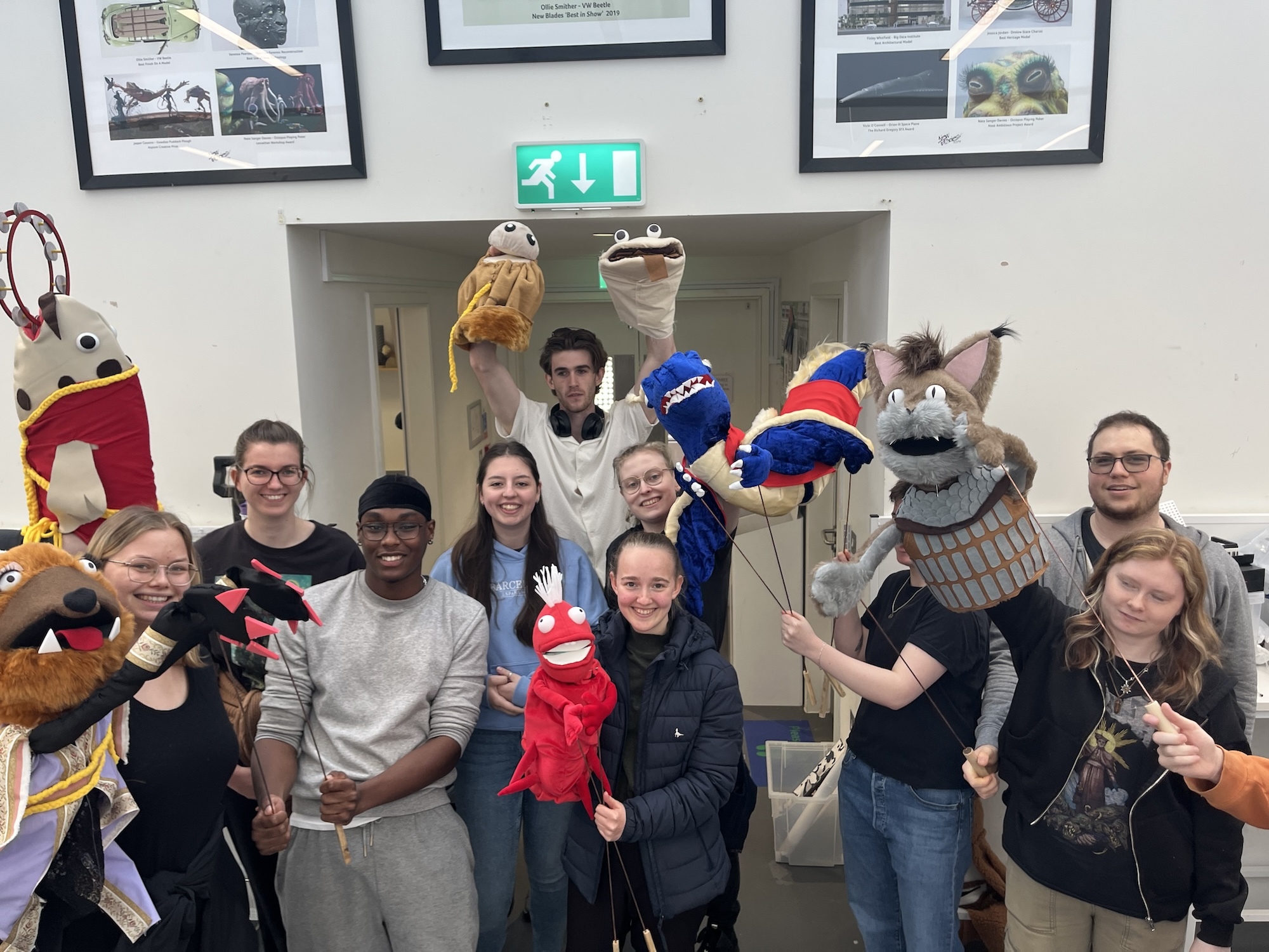A group of BA (Hons) Modelmaking students posing with various puppets in a modelmaking studio at Arts University Bournemouth.