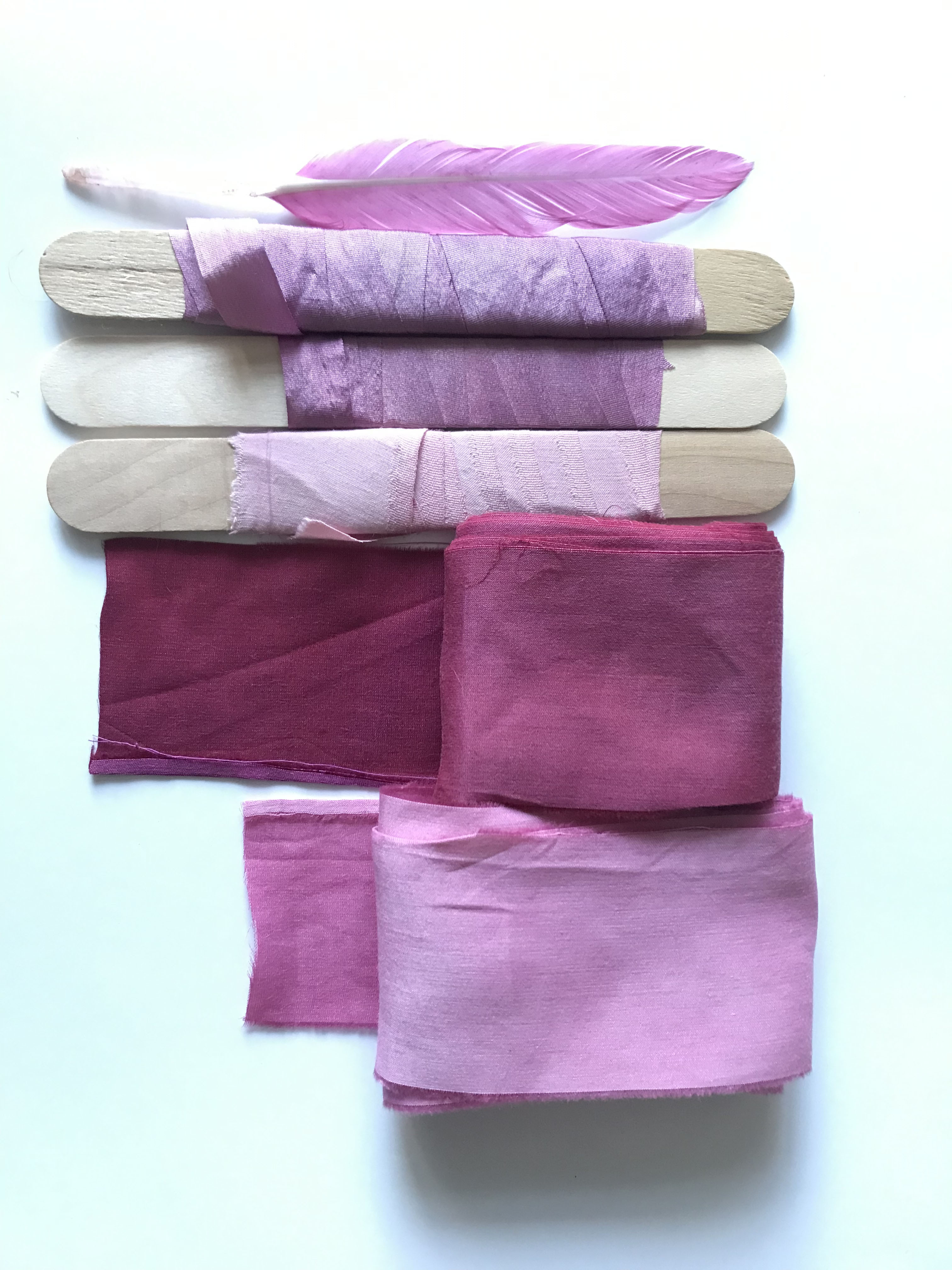 Wooden sticks wrapped with purple fabric strips and loose purple textile pieces arranged vertically on white background.