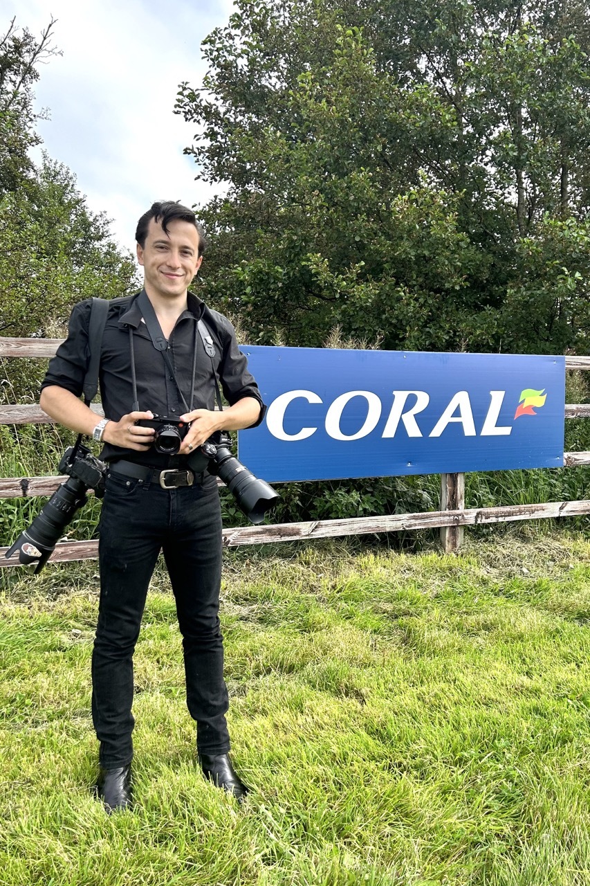 Gabriel Bush stood outside with his camera, in front of a 'Coral' logo.
