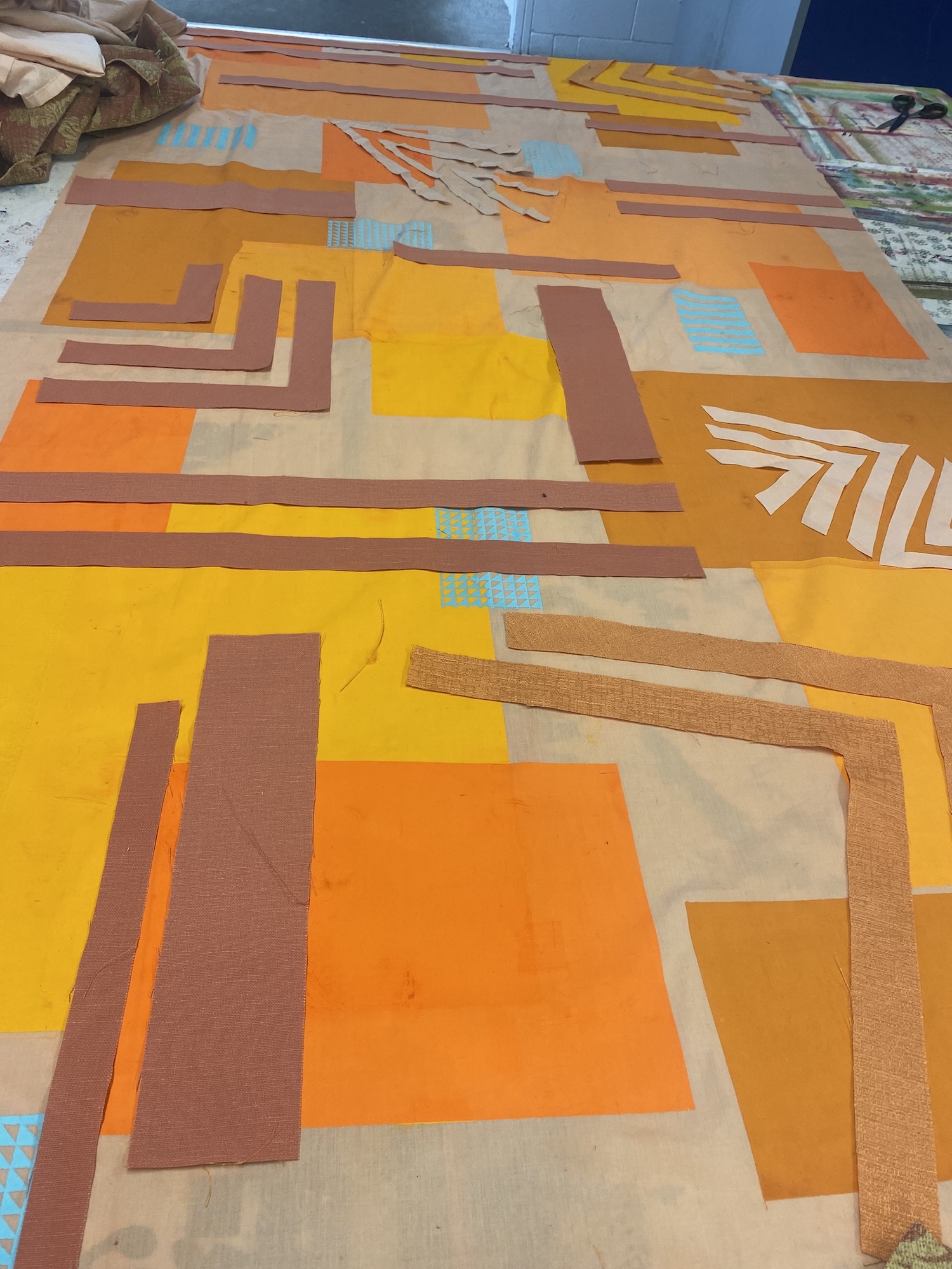 Abstract geometric composition with overlapping rectangular shapes in yellow, orange, brown, and beige tones arranged on flat surface.