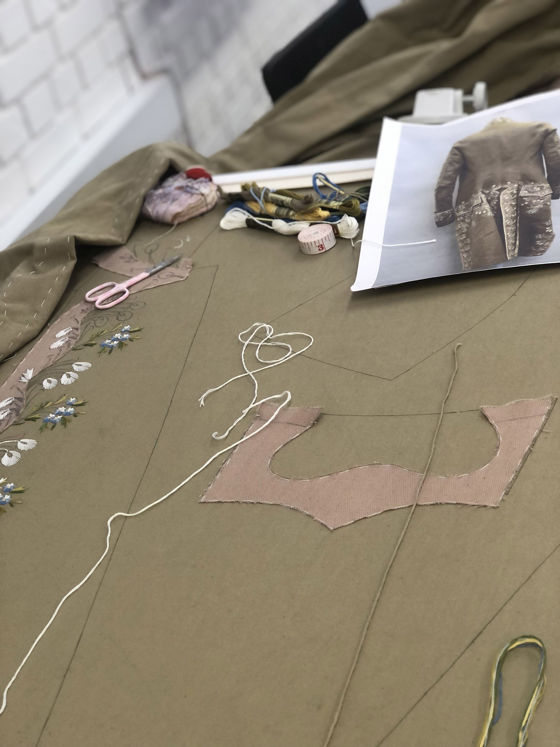 Materials used for embroidery laid out, including thread, scissors and reference image of a jacket