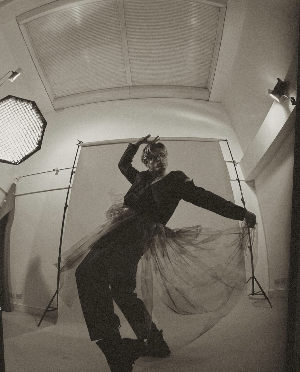 Black and white photo of dancer N Kuzmin posing while holding out a pleat of a gauze skirt, a garment that is part of the 'Happy Hour' collection by J Mitchener.