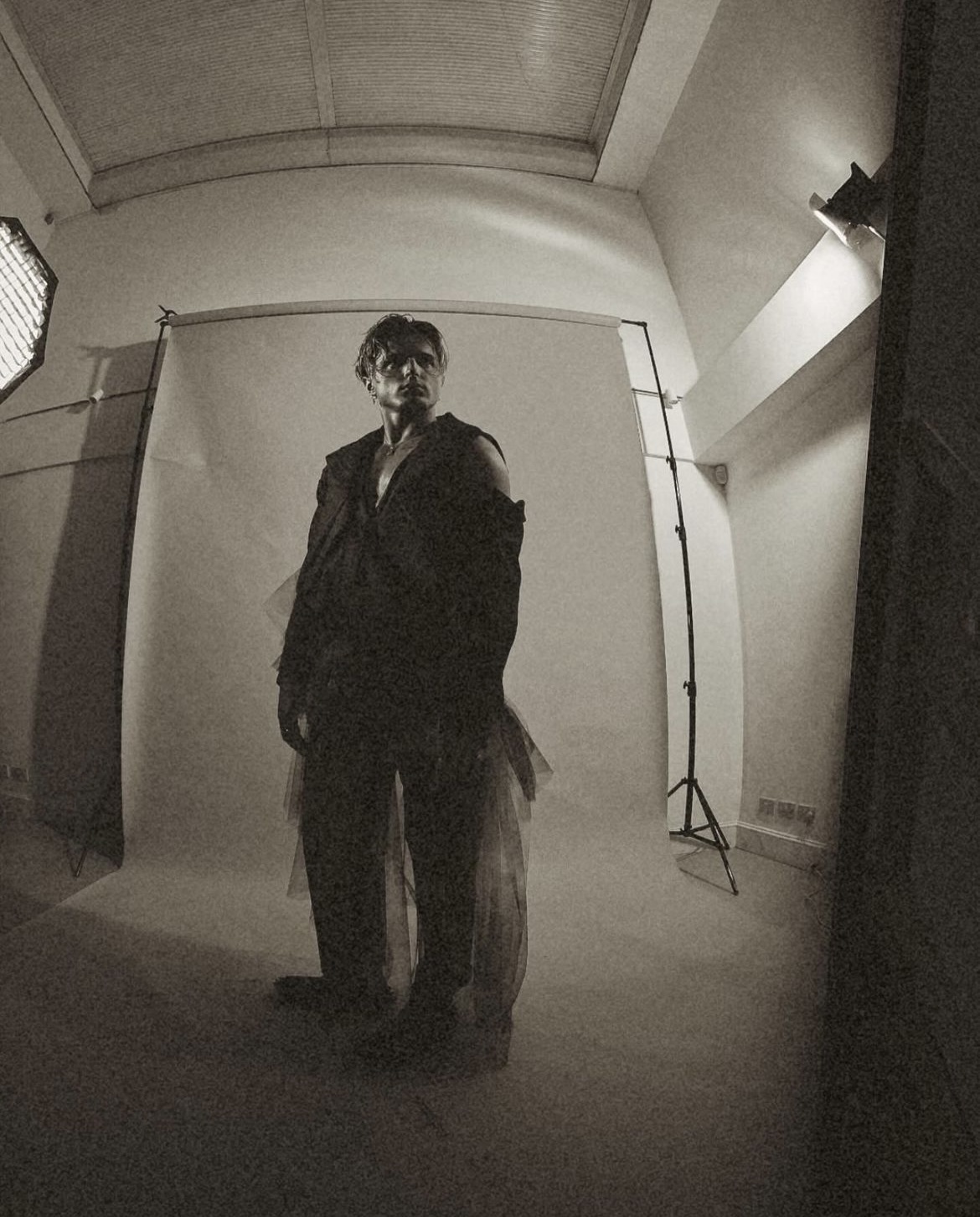 Black and white photo of dancer N Kuzmin standing and posing for a photo while wearing a garment from J Mitchener's collection "Happy Hour".