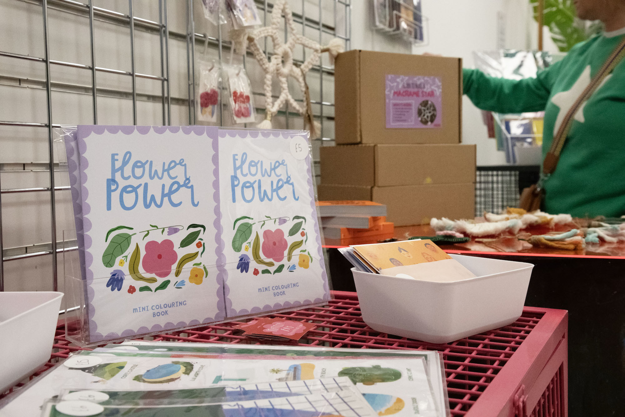 Mini colouring books on display at the #AUBMakers pop-up shop. The books have a colourful flower illustration on the front cover, and text reading "Flower Power".