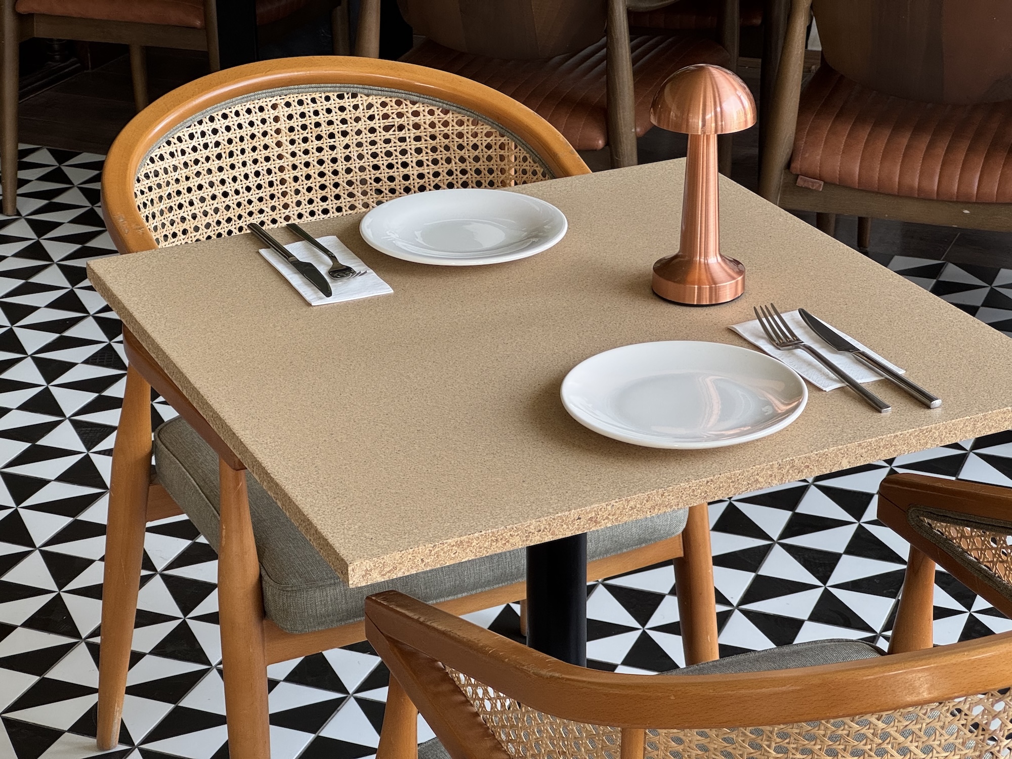 A square table in a restaurant with plates, cutlery and a lamp. The table is made from Pit-Board sustainable material.