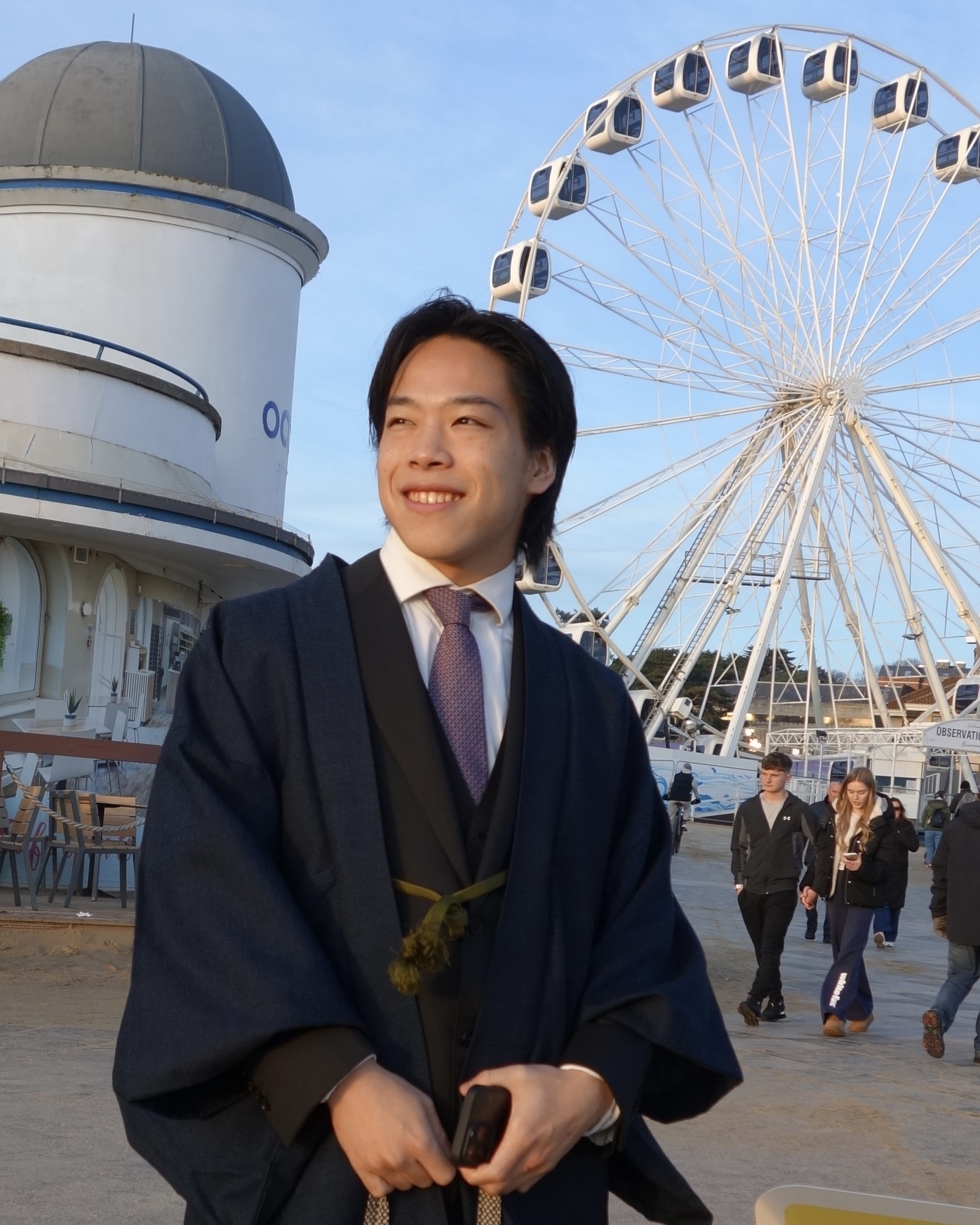 Seiji Suzuki stood at Bournemouth seafront wearing a blue gown, ferris wheel and oceanarium in the background.