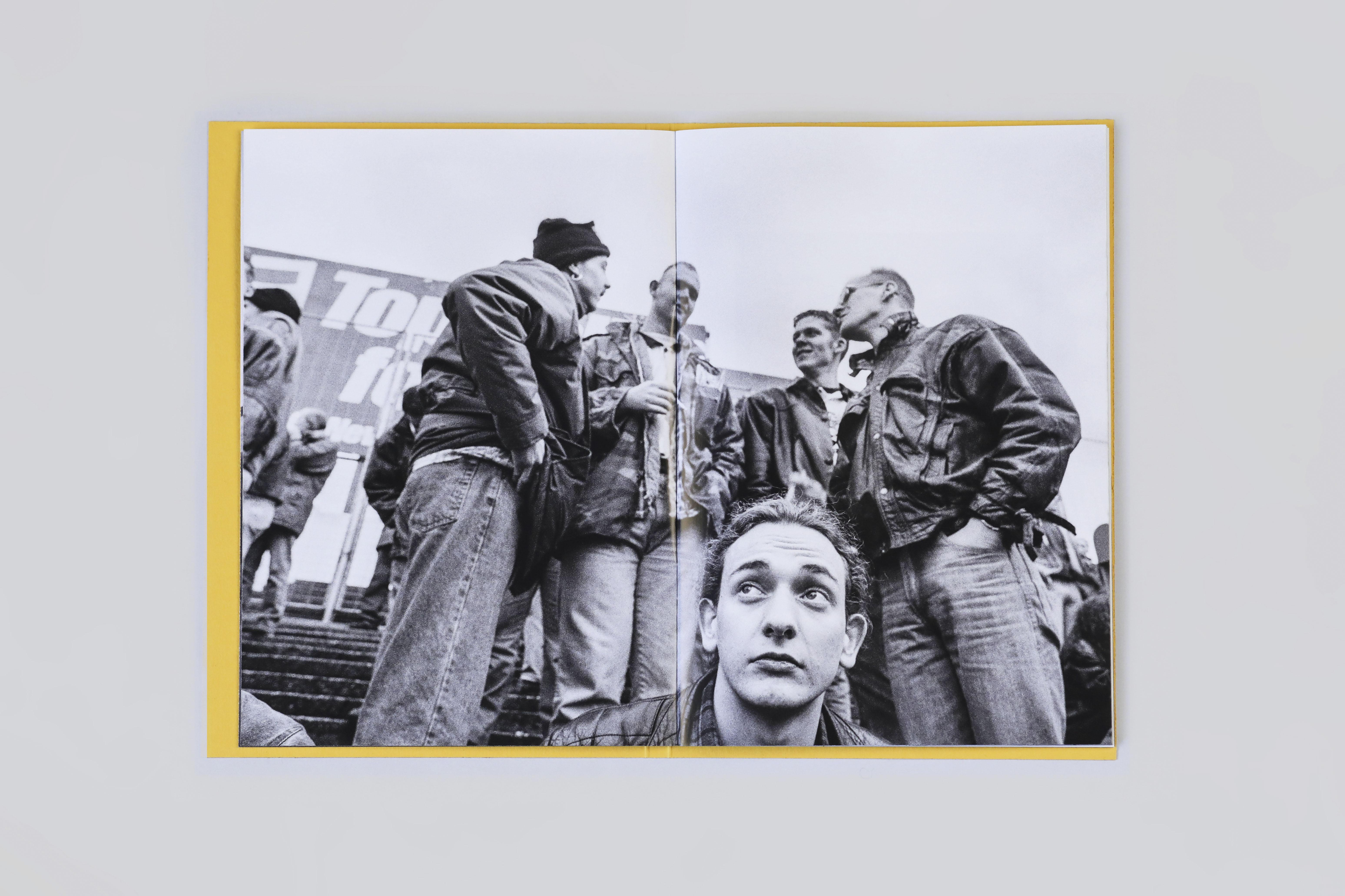 A book open to a double-page spread showing a black and white photo of a man seated with four other men stood talking behind him.