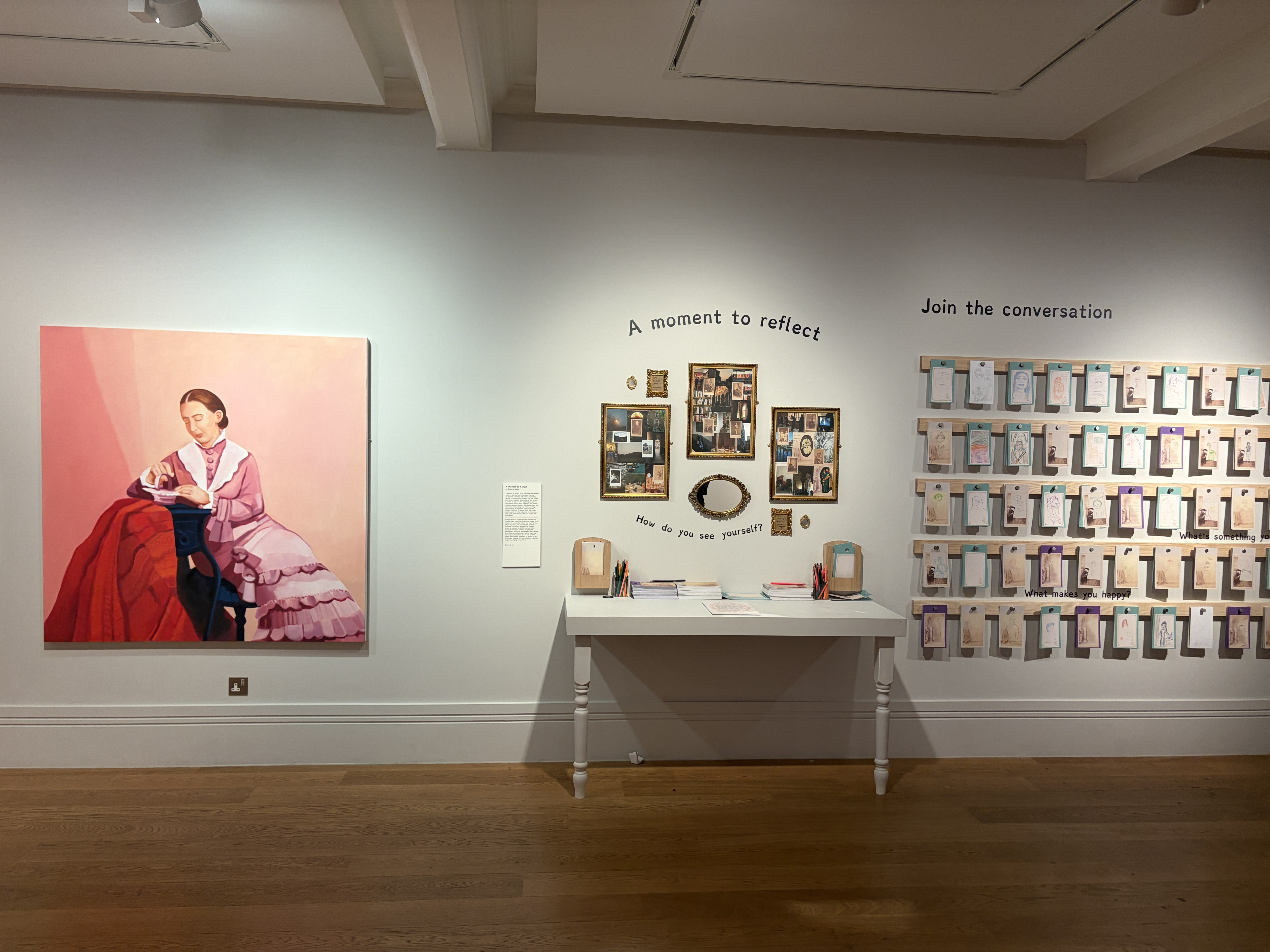 A gallery wall with a large portrait painting on the left, a small display table in the centre, and a grid of hanging cards on the right beneath the words “Join the conversation”.