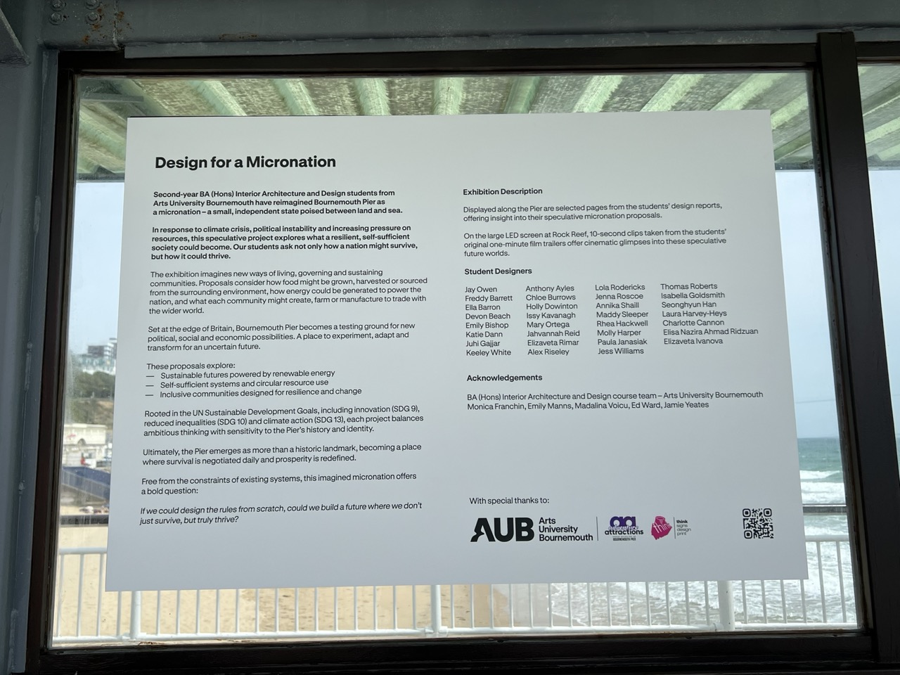 White display with paragraphs explaining the 'Design for a Micronation' exhibition, beach in background.