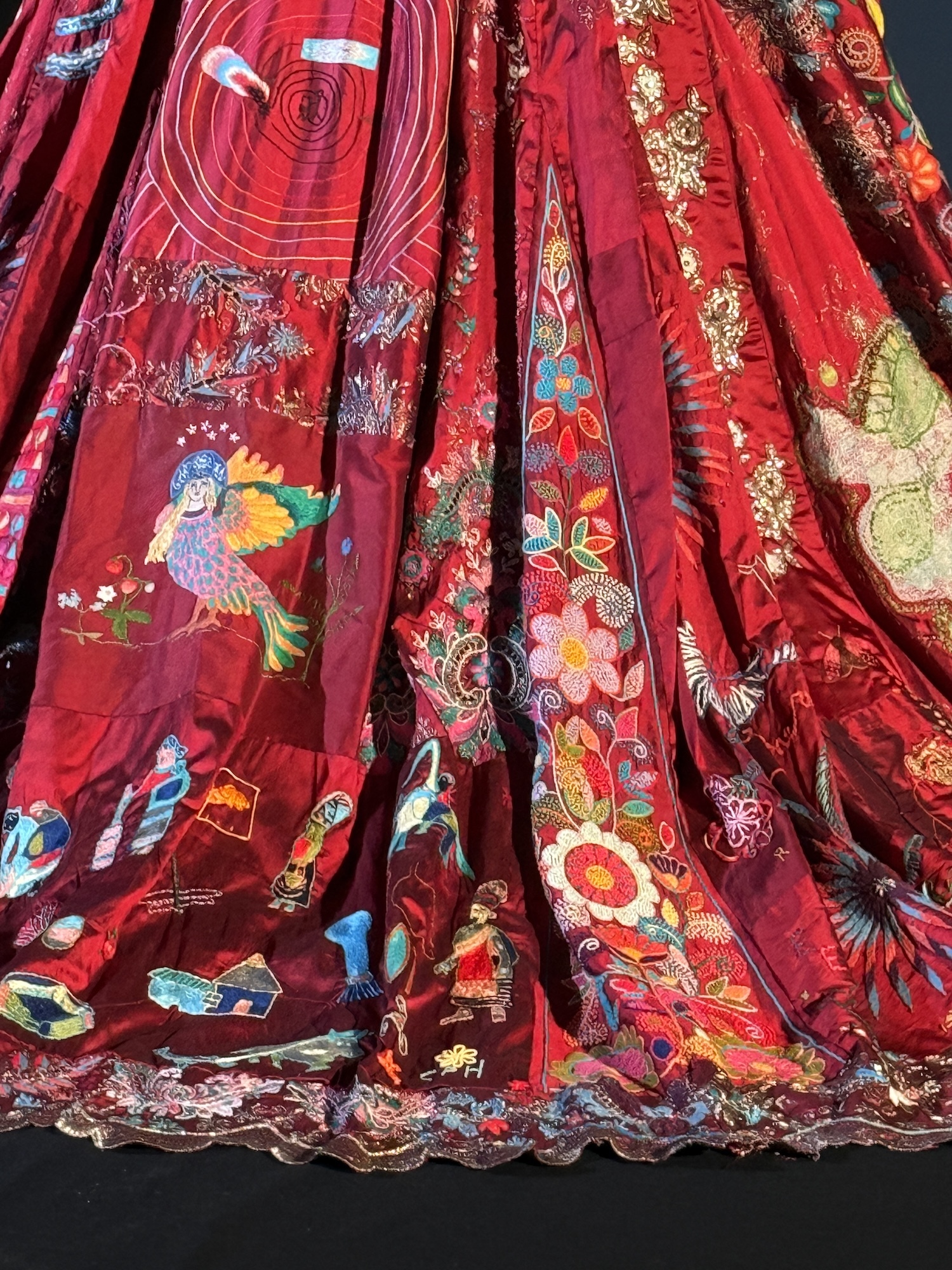Red silk garments with colourful embroidered patterns including birds, flowers, and geometric designs in blues, yellows, and greens.
