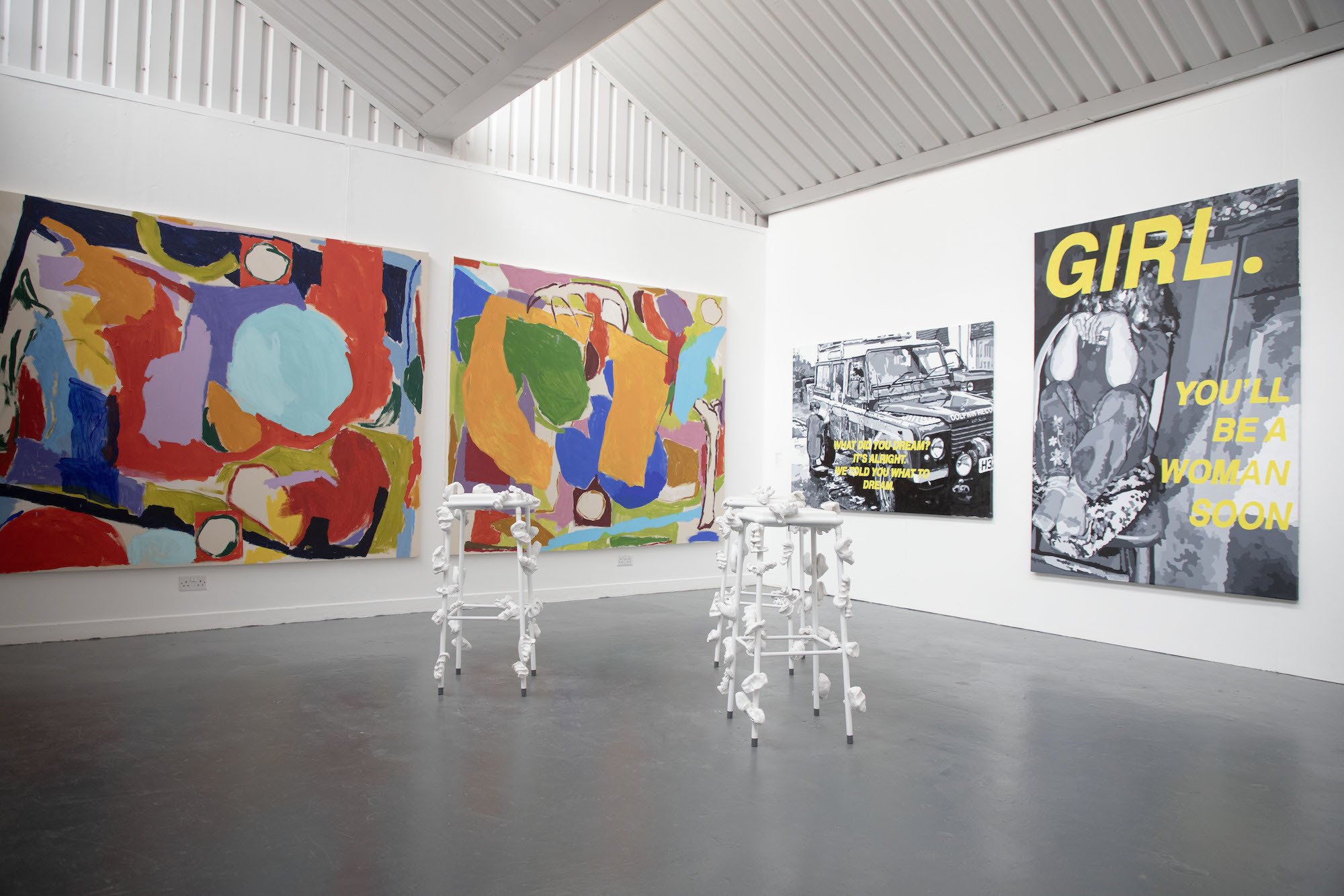 Corner of a gallery space on AUB Campus, with four artworks displayed on the walls and two sculptures in the middle of the floor.