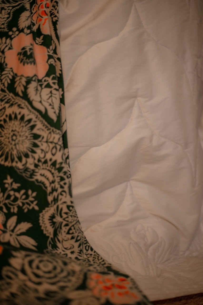Crumpled white fabric beside patterned textile with green paisley designs, floral motifs, and orange accents on cream background.
