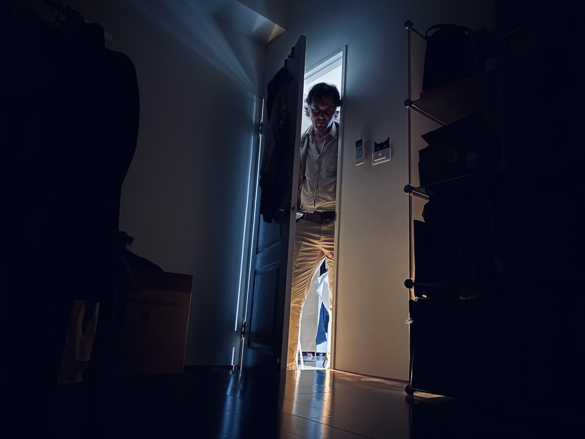 Film still of a person with a vindictive expression stepping through a door into a dark room.
