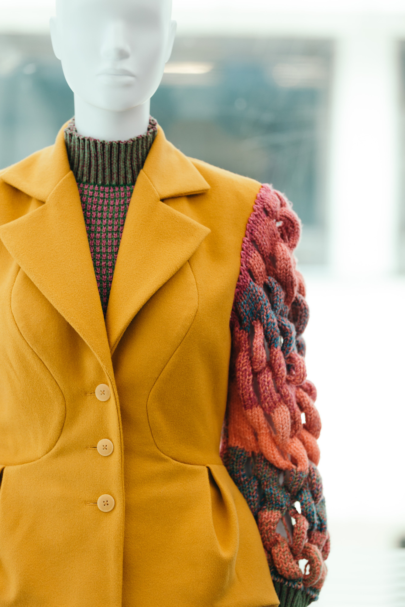 Mannequin wearing a yellow coat with red and blue fabric-woven arms.