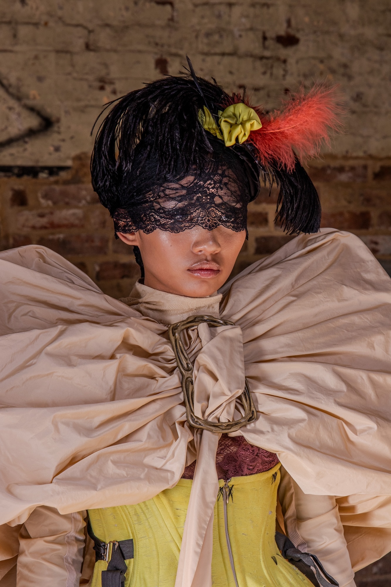 Close-up of a model wearing a black lace masquerade mask and headdress and a pale gold puffy coat/cape.