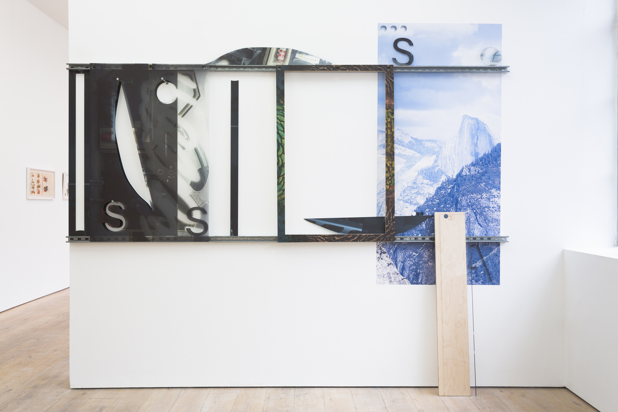 Abstract photographic works, one panel with mountain imagery, displayed on a gallery wall. A large ruler is leant up against the wall on the right.