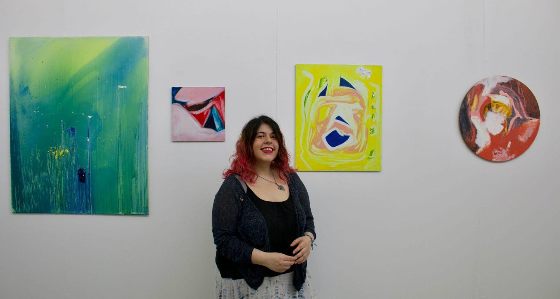 M Sabanci standing in front of four pieces of artwork displayed on a gallery wall.