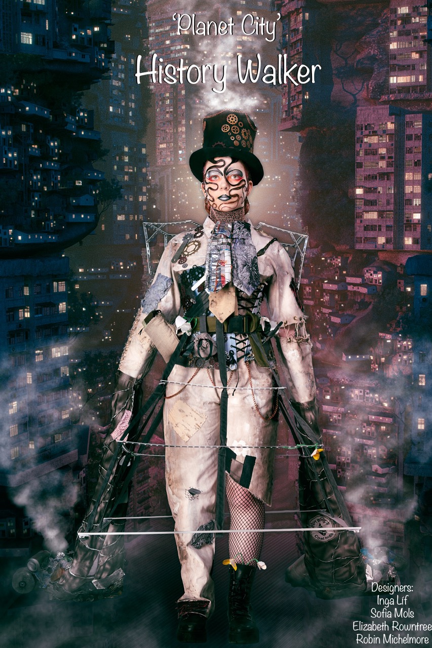 A model stands in a futuristic costume featuring a top hat, mask, and elaborate clothing, set against a backdrop of a cityscape with tall buildings. The design includes unusual accessories and a structured, geometric frame.