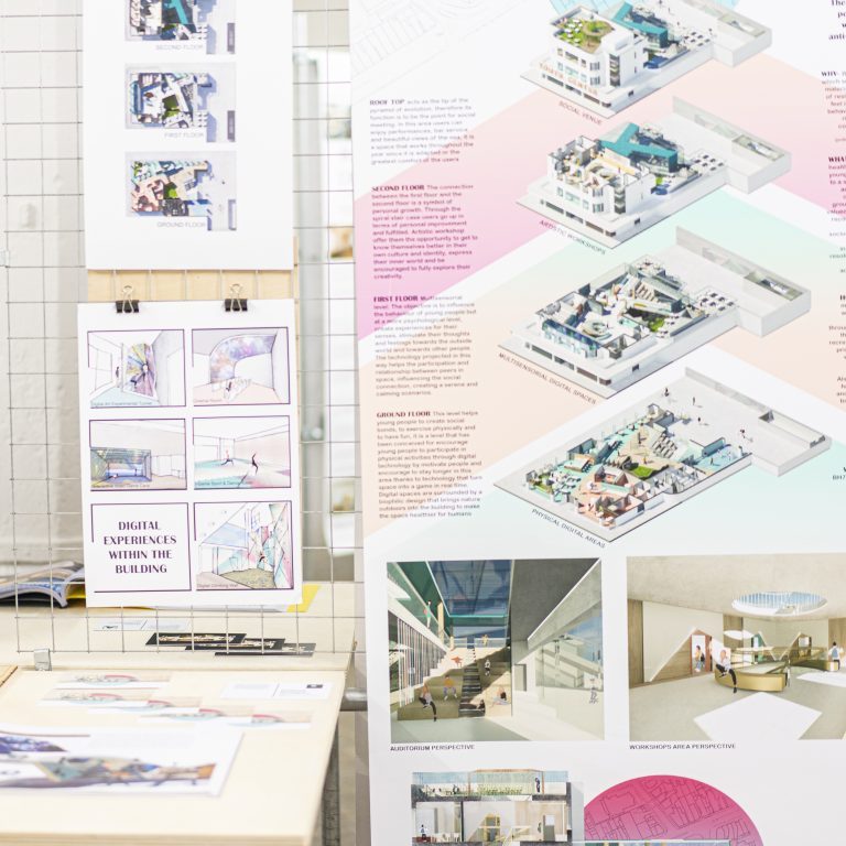 Diagrams and blocks of text on several sheets of paper, hanging on display by a table.