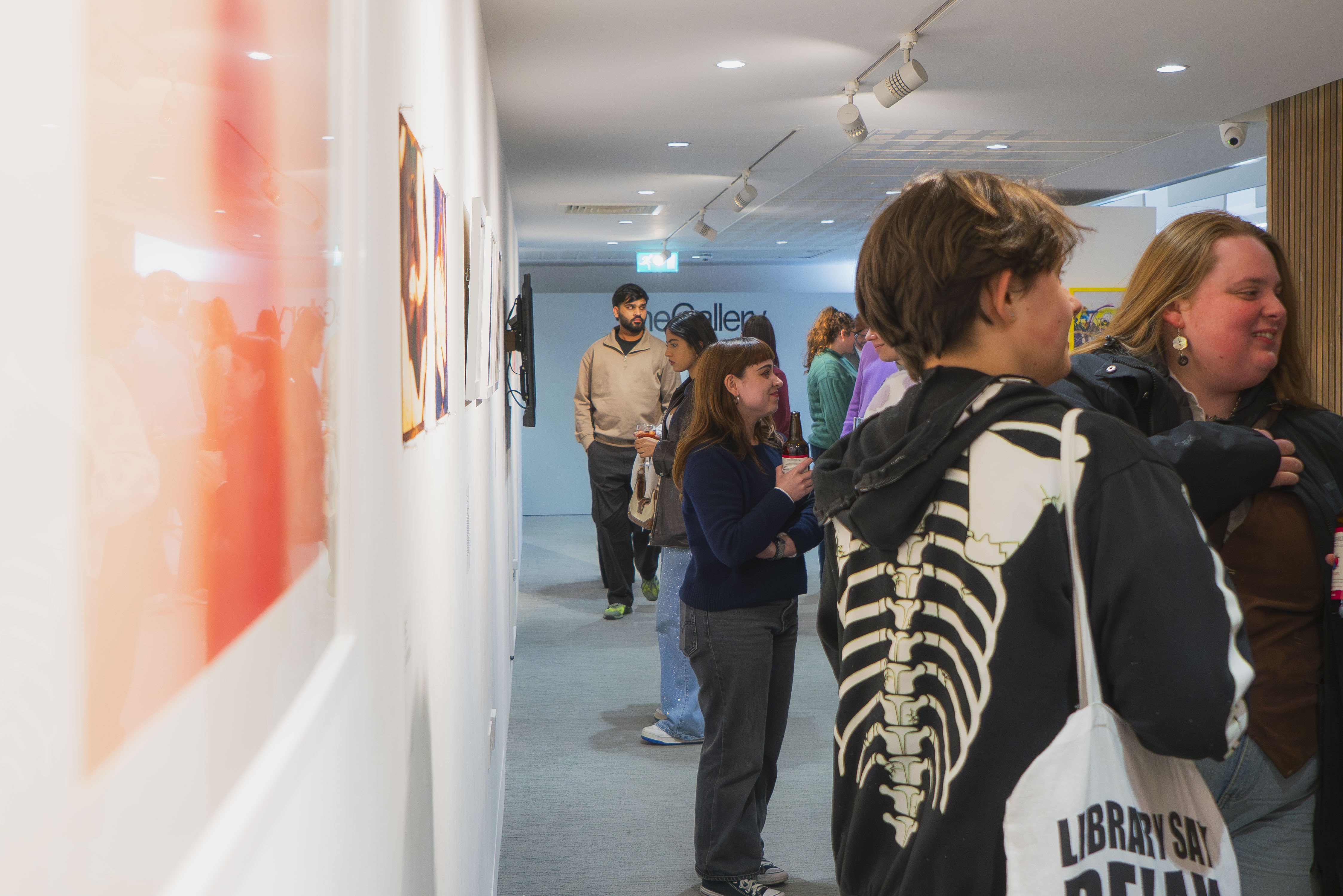 People viewing artwork in white gallery space with track lighting and framed pieces on walls