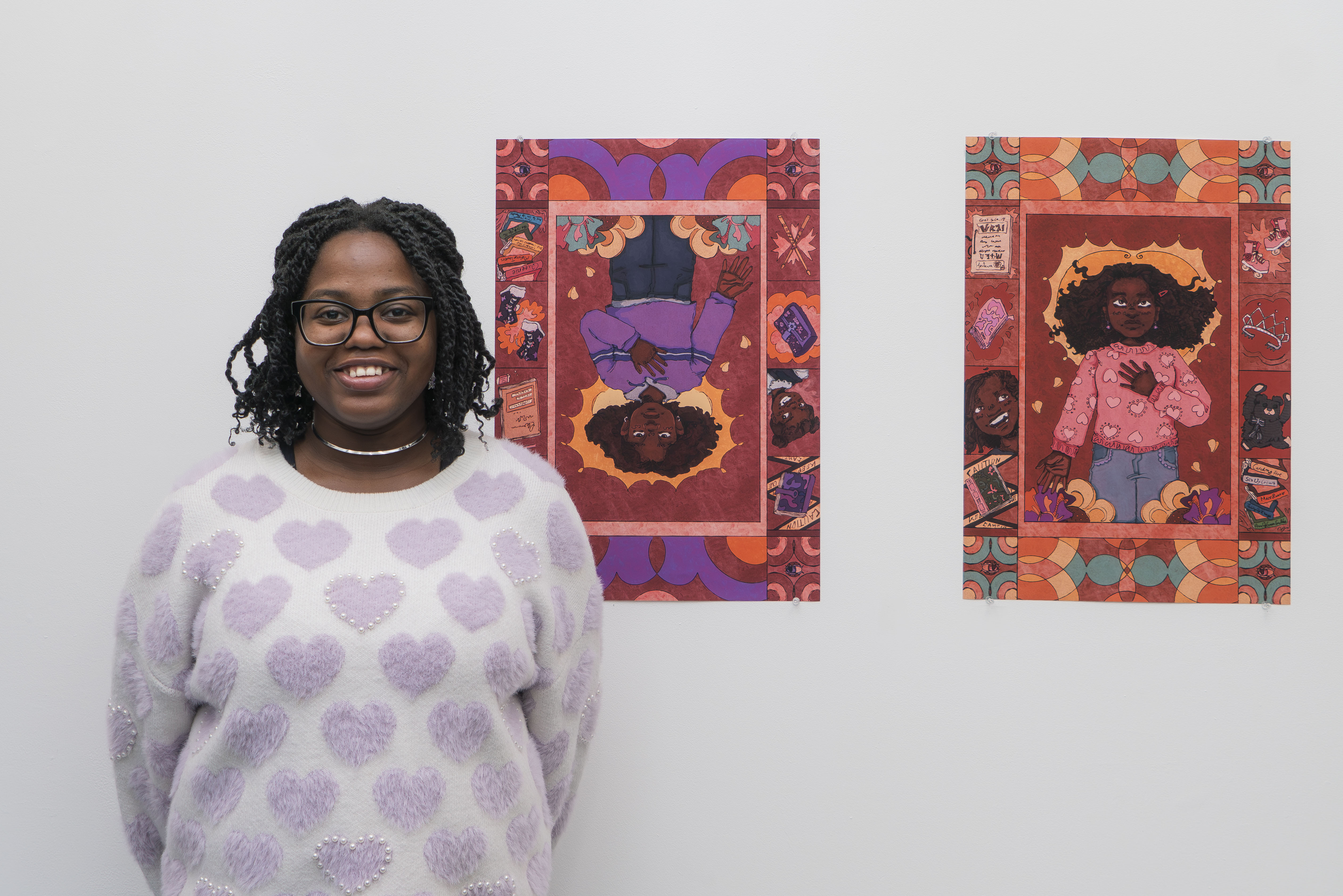 Student with glasses in purple patterned top stands before two colourful illustrated artworks, self-portraits, featuring geometric patterns.