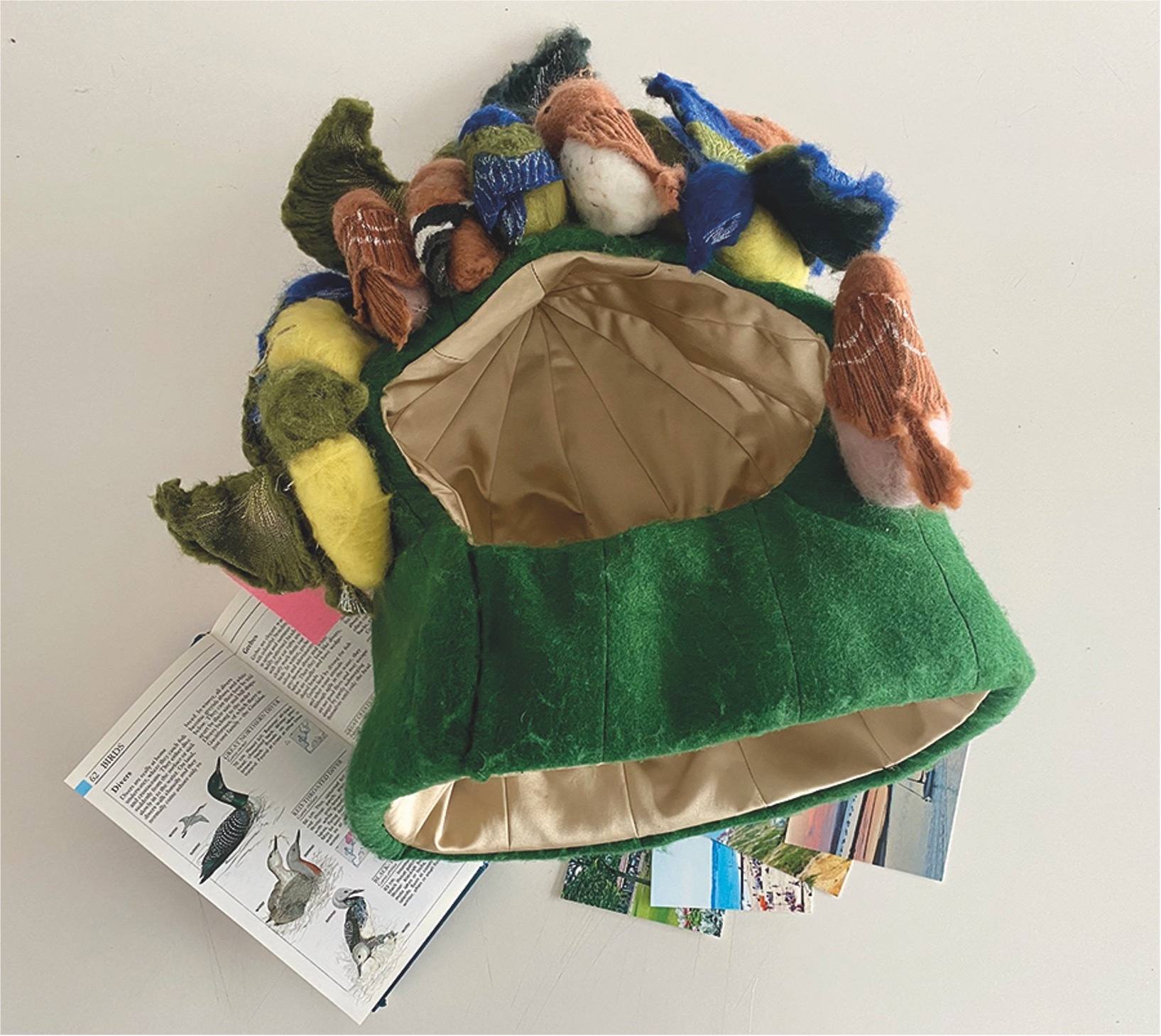 Green fabric bag overflowing with colourful yarn balls in blue, yellow, brown, and orange hues, sitting atop newspaper pages.