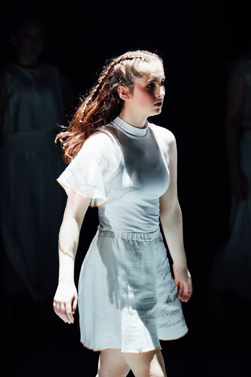 Young woman with braided auburn hair wearing pale blue dress, looking to the right against dark background with dramatic lighting.