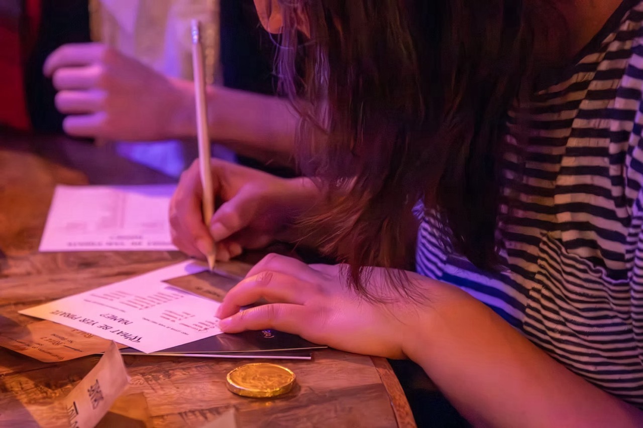 Close-up of a person writing on paper on a wooden table, moody warm and purple lighting.