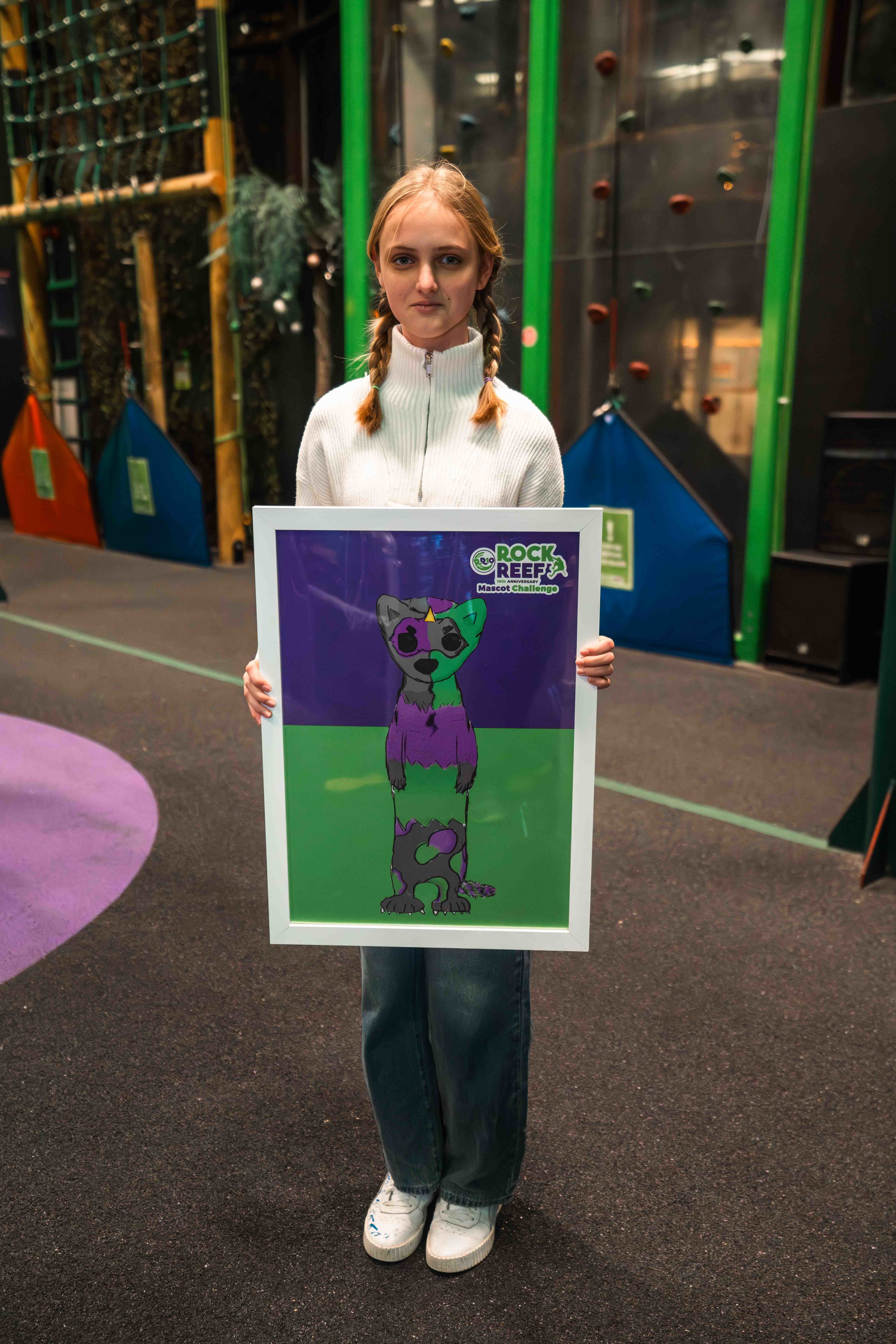 I. Kaczynska holding a poster showing an illustration of a green and purple otter mascot at RockReef on Bournemouth Pier.