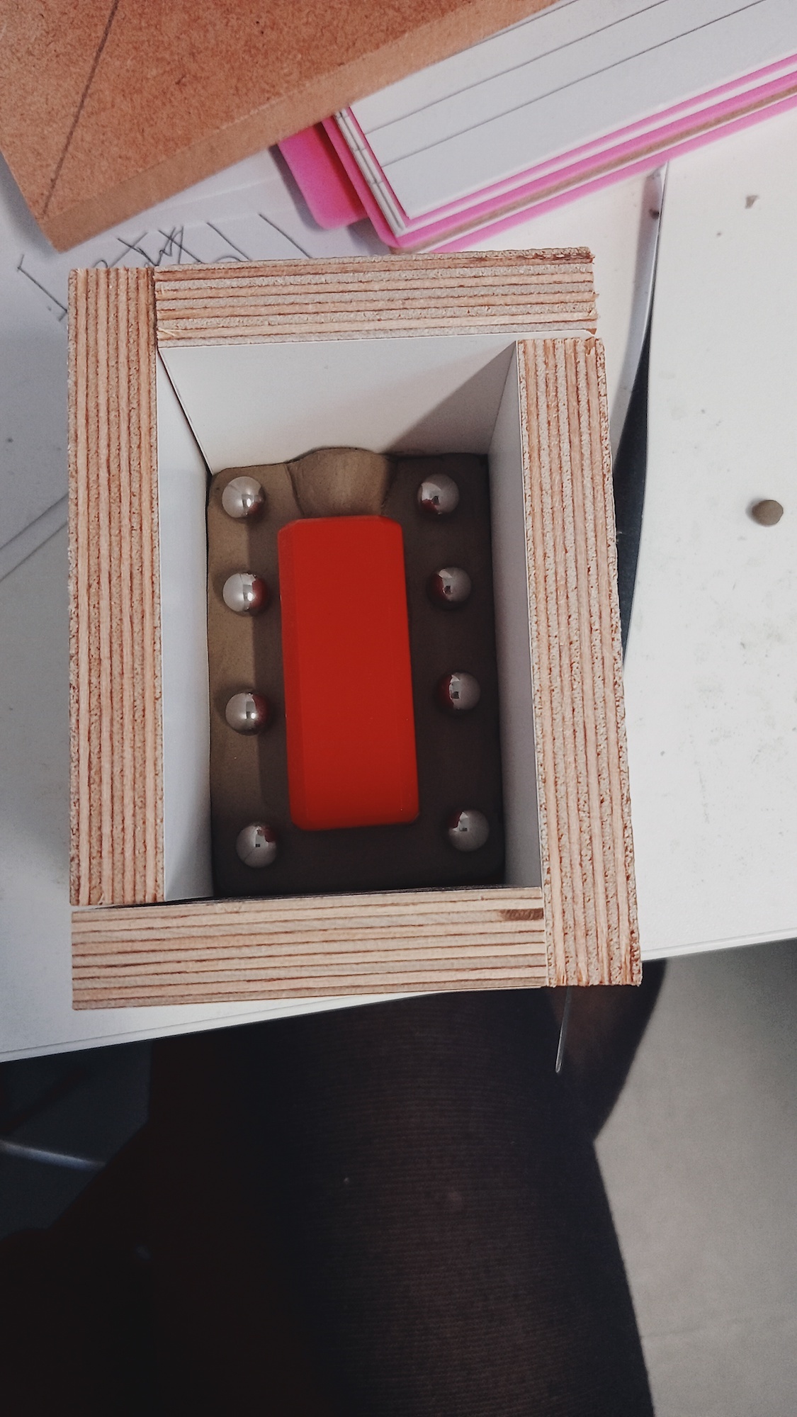 Wooden box holding a red object and metal ball bearings.