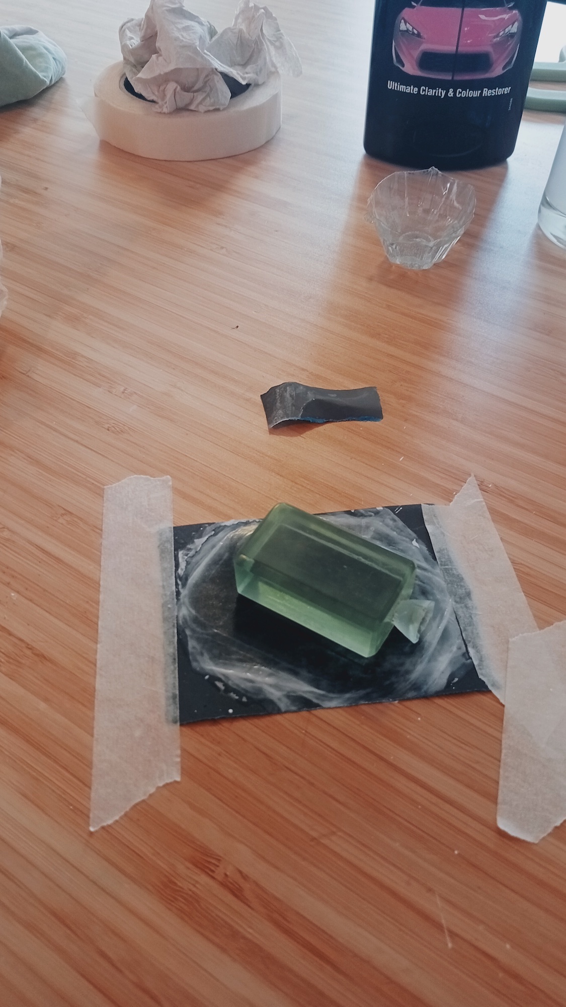 Green glass bottle on a taped-down black piece of card, wooden table.